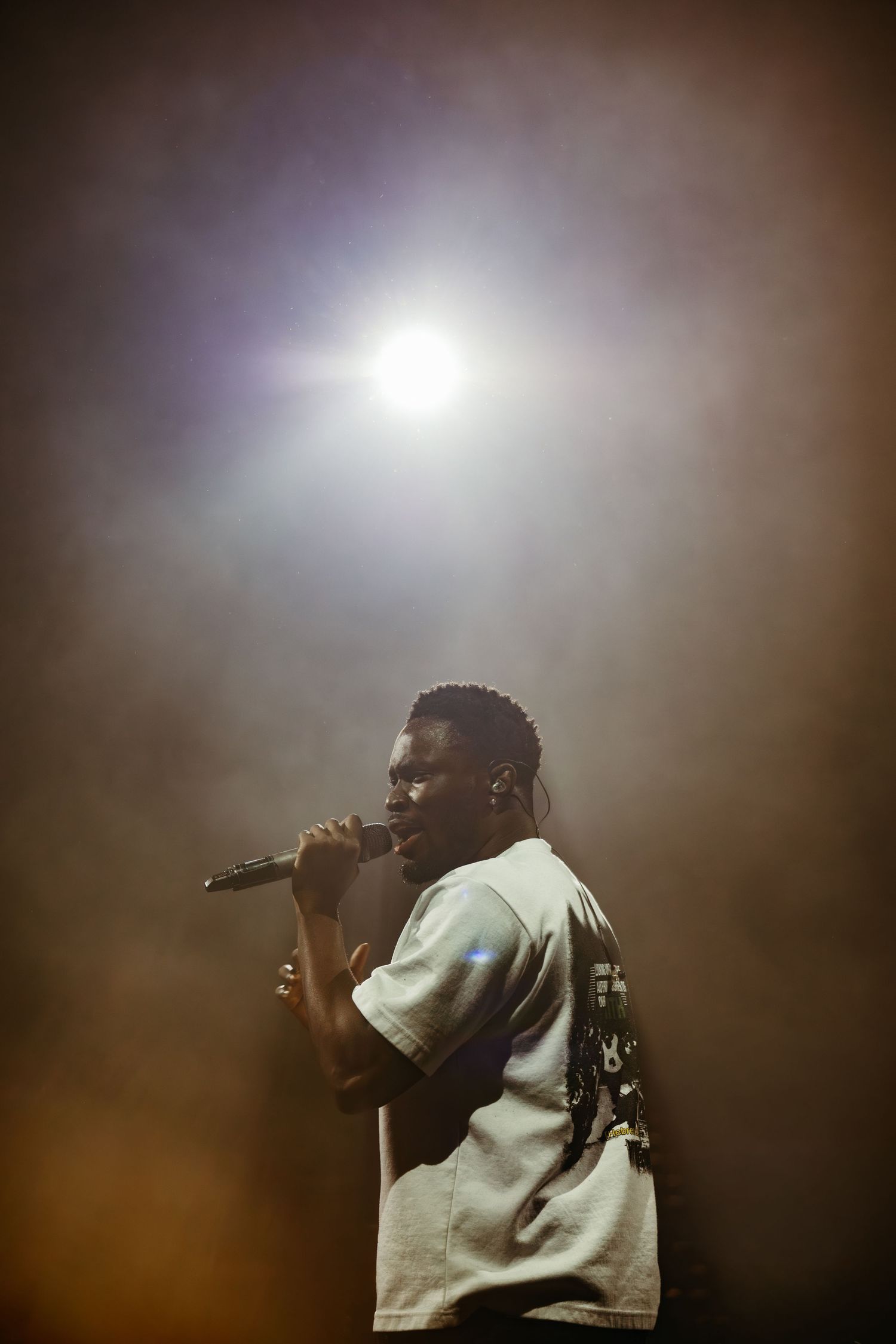 A performer sings into a microphone on a smoky stage under a bright spotlight.