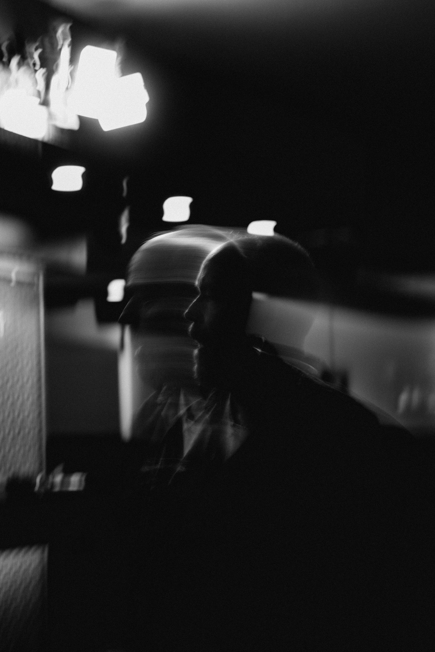 Blurry black and white portrait of a bald man in profile with bright lights in background.
