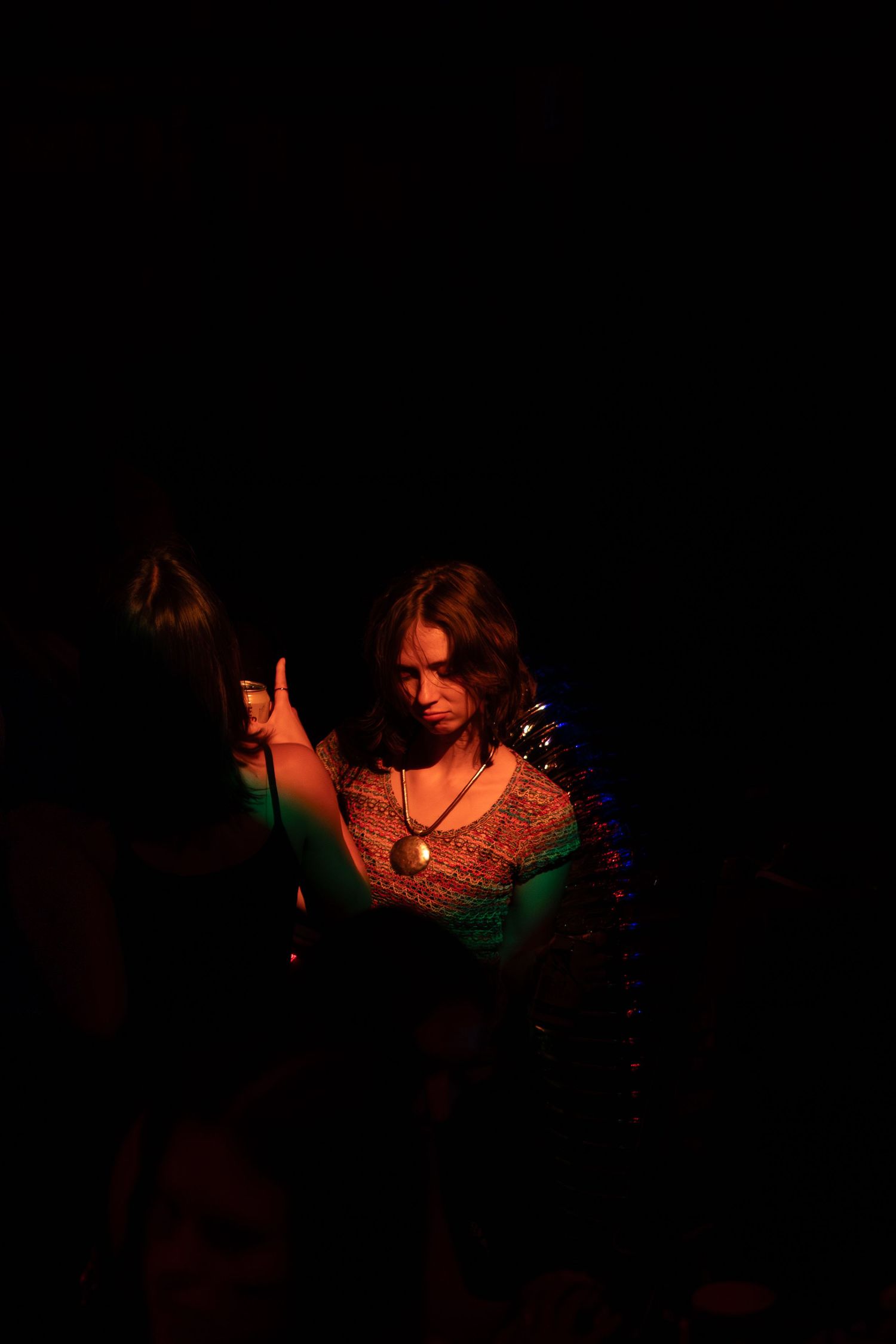 Woman with necklace illuminated by warm red light in a dark setting.