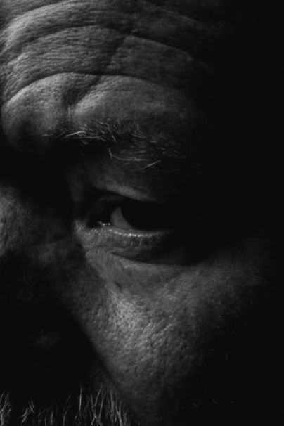 Close-up black and white portrait of an elderly man's eye, showing deep wrinkles and aged skin texture.