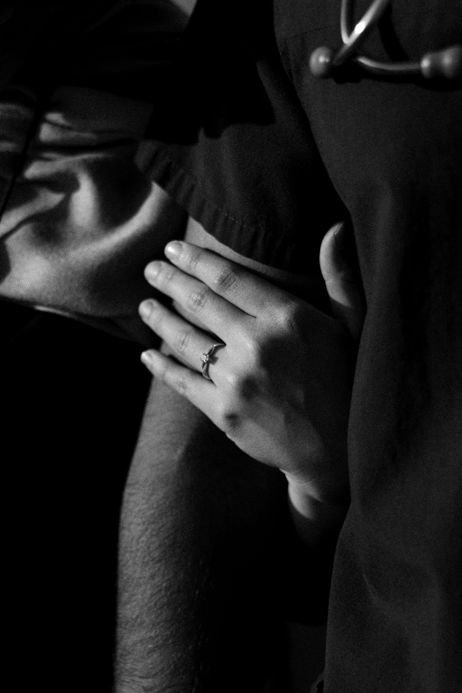Black and white photo of a woman's hand with an engagement ring resting on a man's arm.