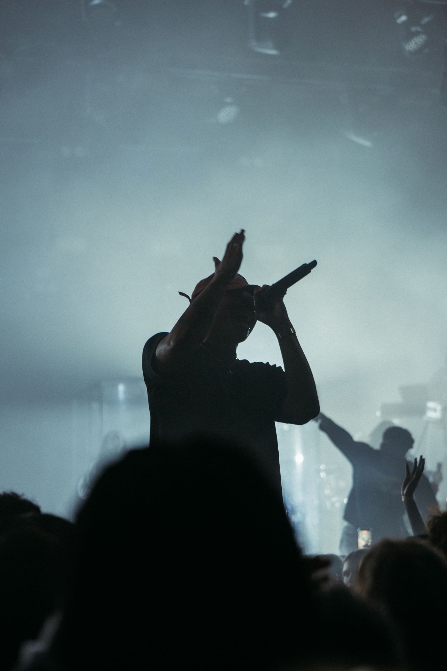 Silhouette of a rapper holding a microphone at a live concert with dramatic foggy stage lighting.