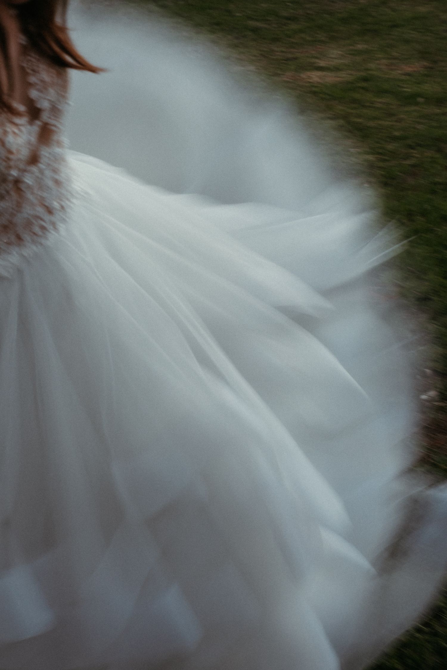 A bride's flowing white tulle wedding gown captured in motion blur outdoors.