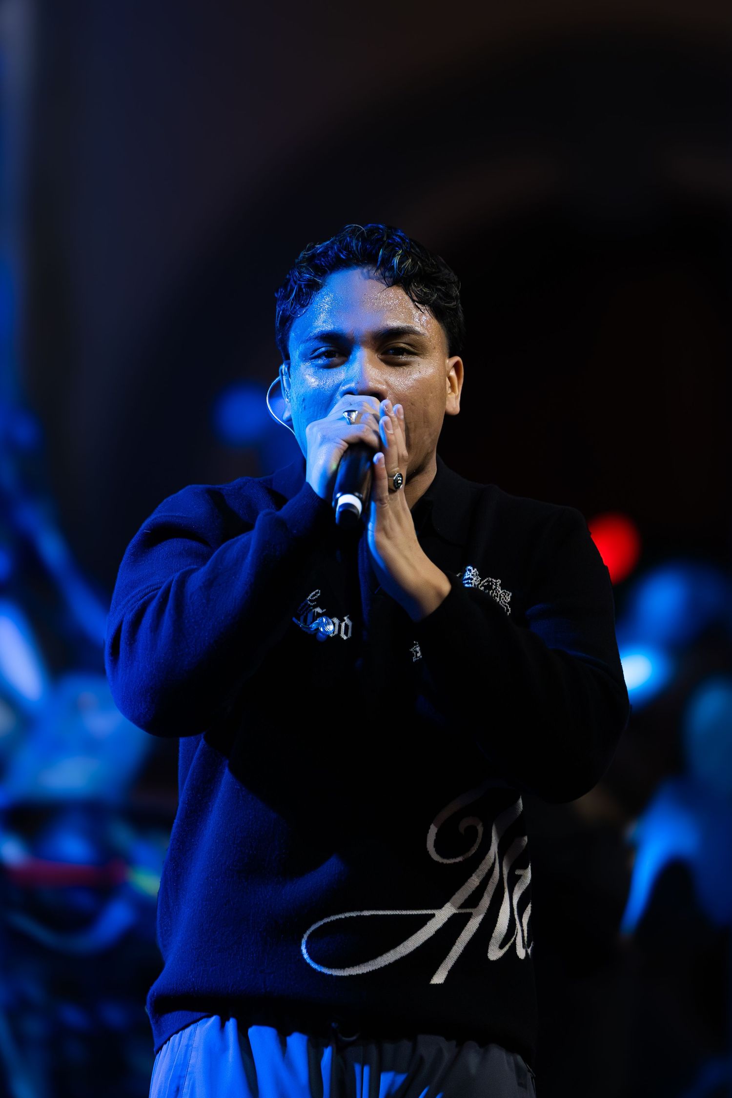 Male singer performing on stage holding microphone with both hands under blue stage lighting.
