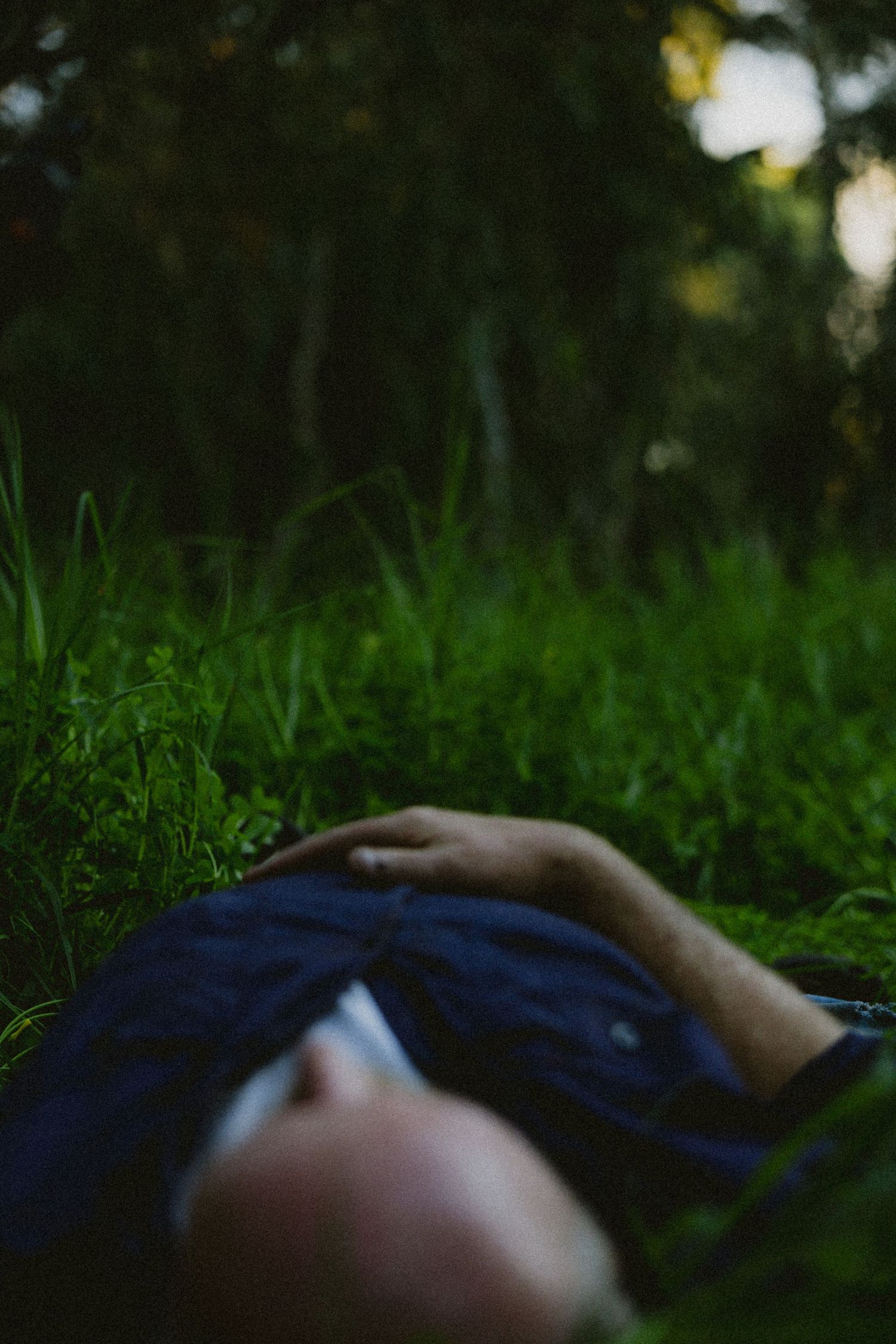 Man lying on his back in green grass surrounded by trees in soft natural light.