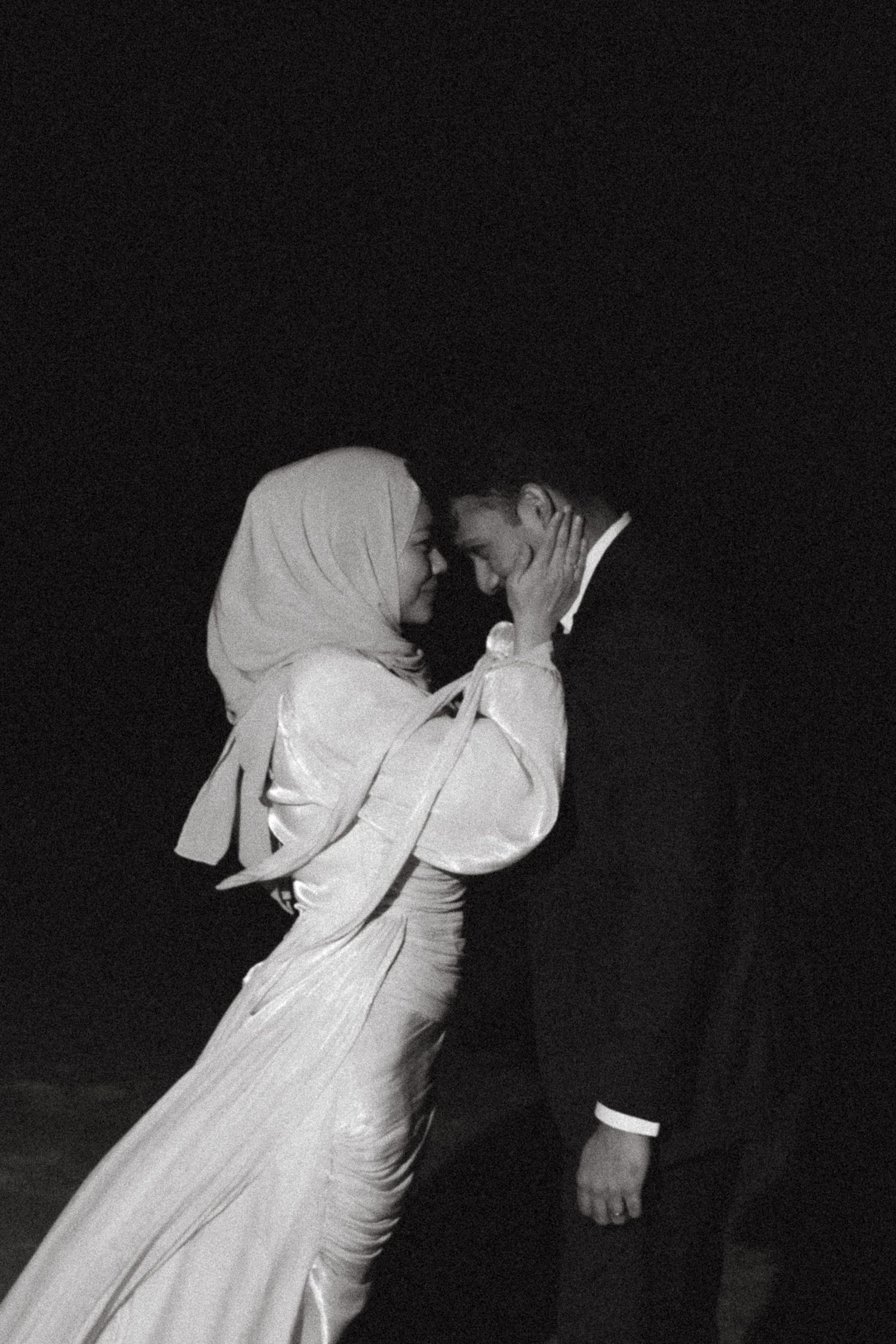 Black and white photo of a bride in hijab and groom sharing an intimate moment during their wedding night.
