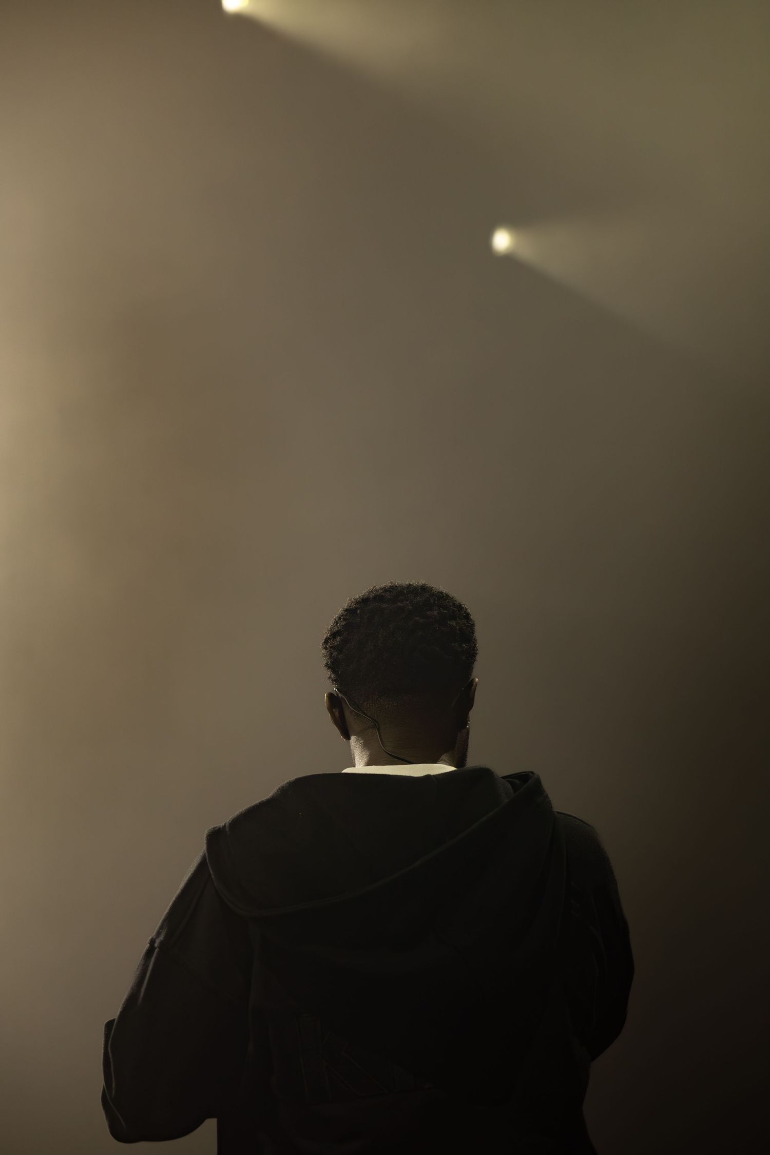 Silhouette of a performer on a smoky concert stage with dramatic spotlights shining overhead.