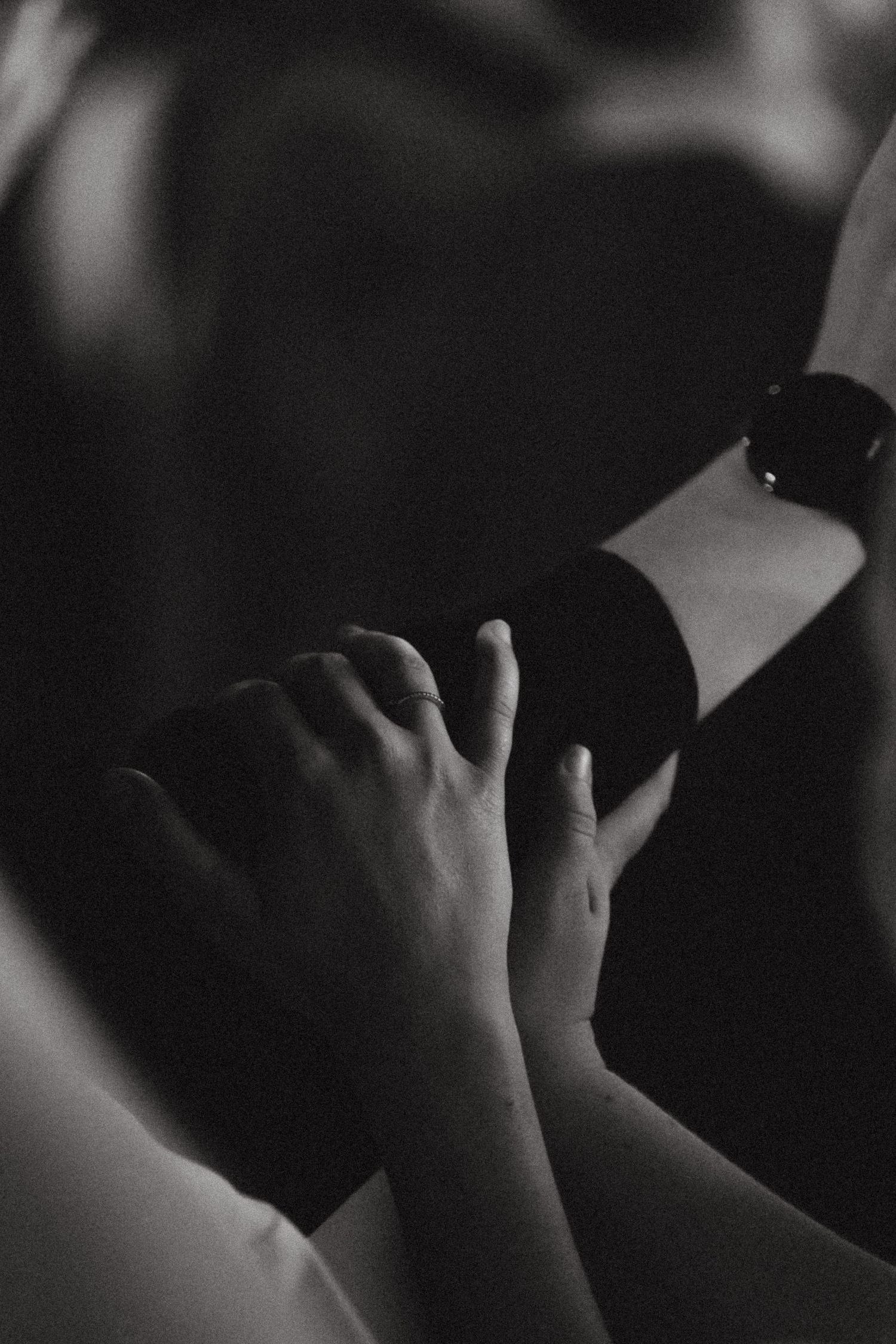 Black and white photo of two hands gently touching, one wearing a watch, in soft dramatic lighting.
