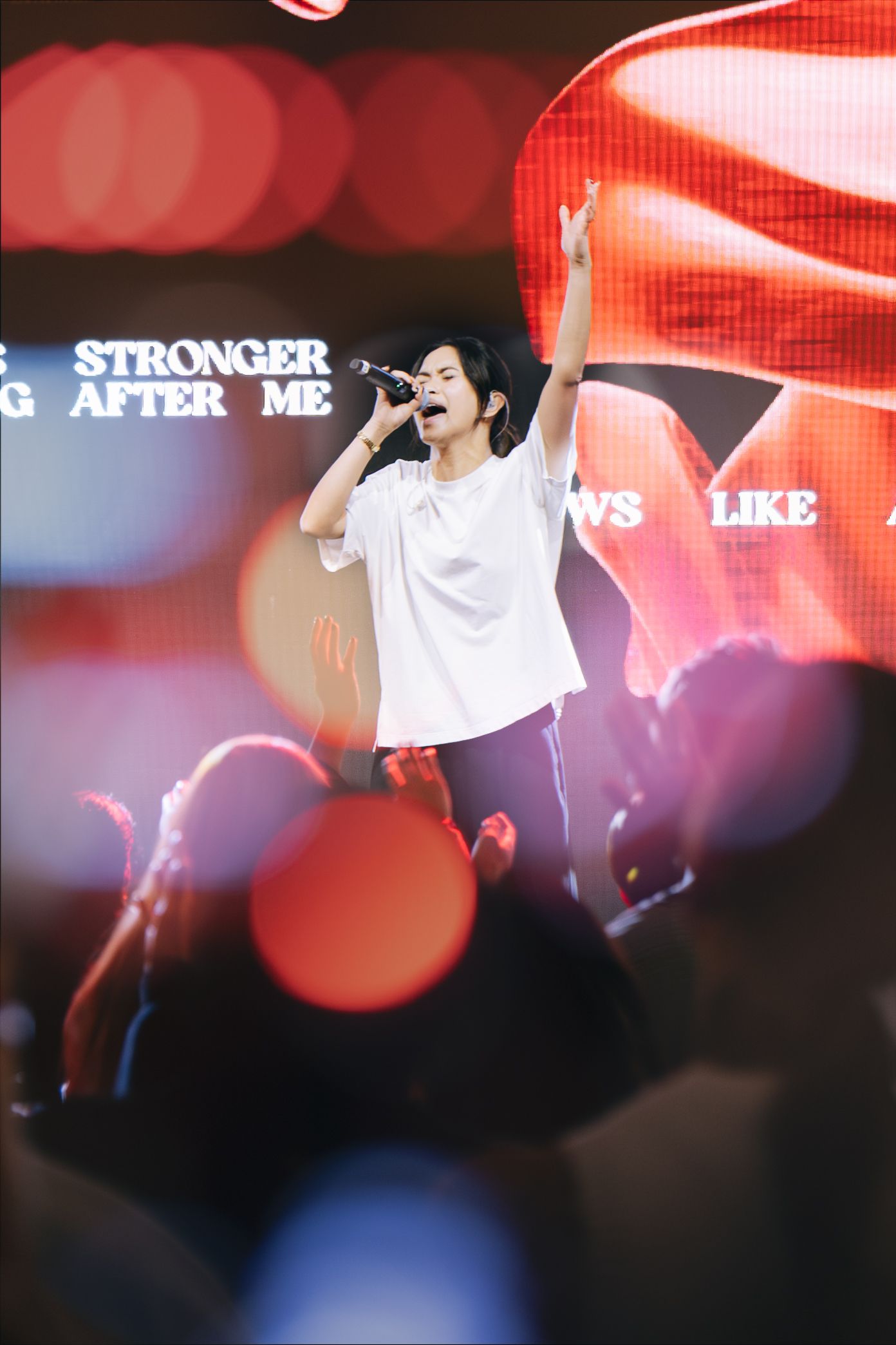 Singer in white t-shirt performing on stage with raised hand at a Christian worship concert.