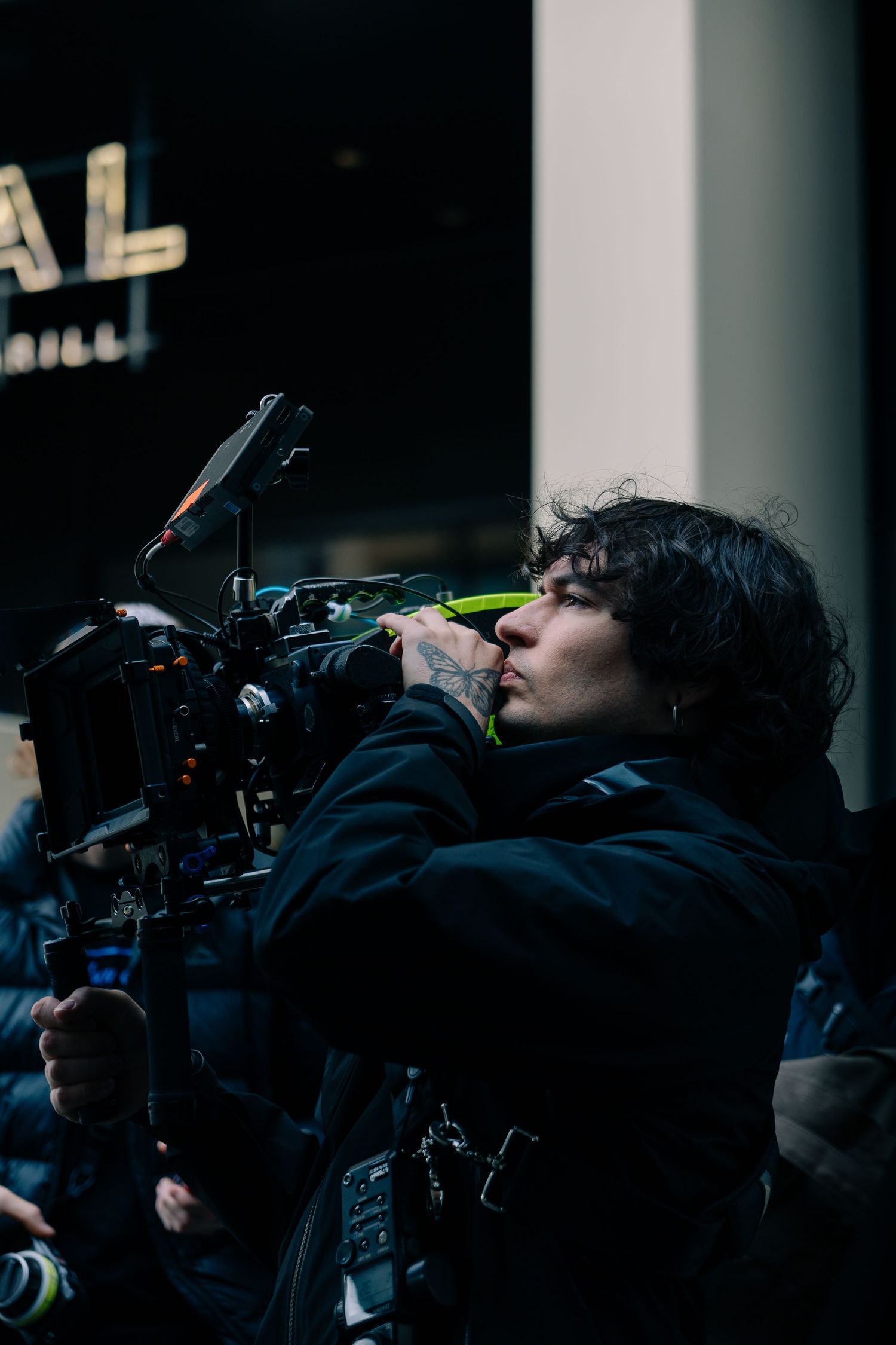 Cinematographer operating a professional film camera rig on a dark urban street location.