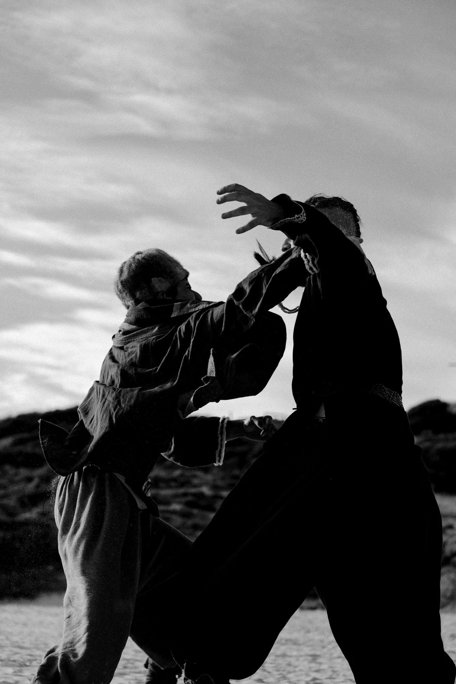 Black and white silhouette of two people sparring in a martial arts fight outdoors.