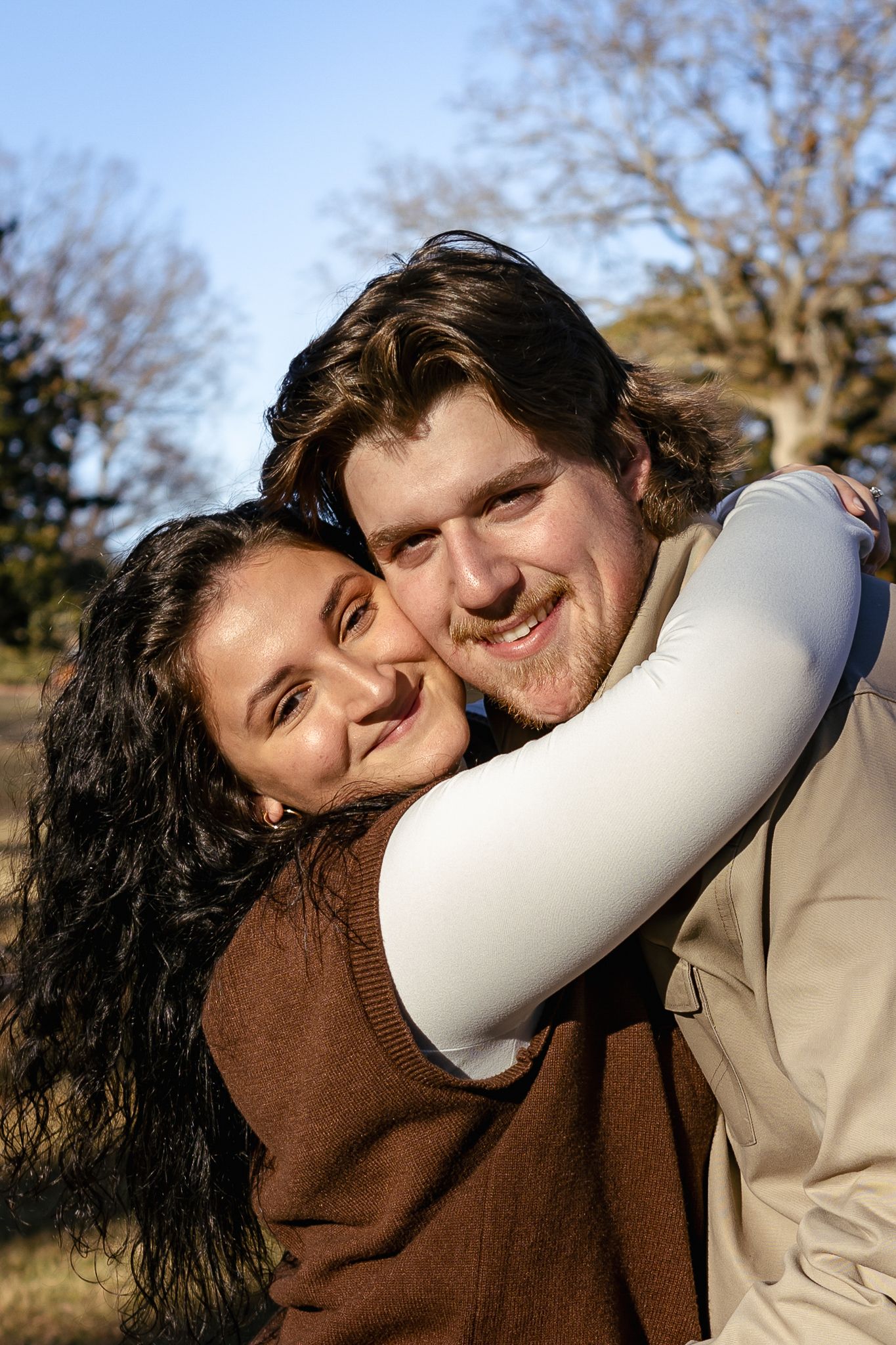 Happy young couple embracing and smiling together outdoors under blue sky with bare winter trees.
