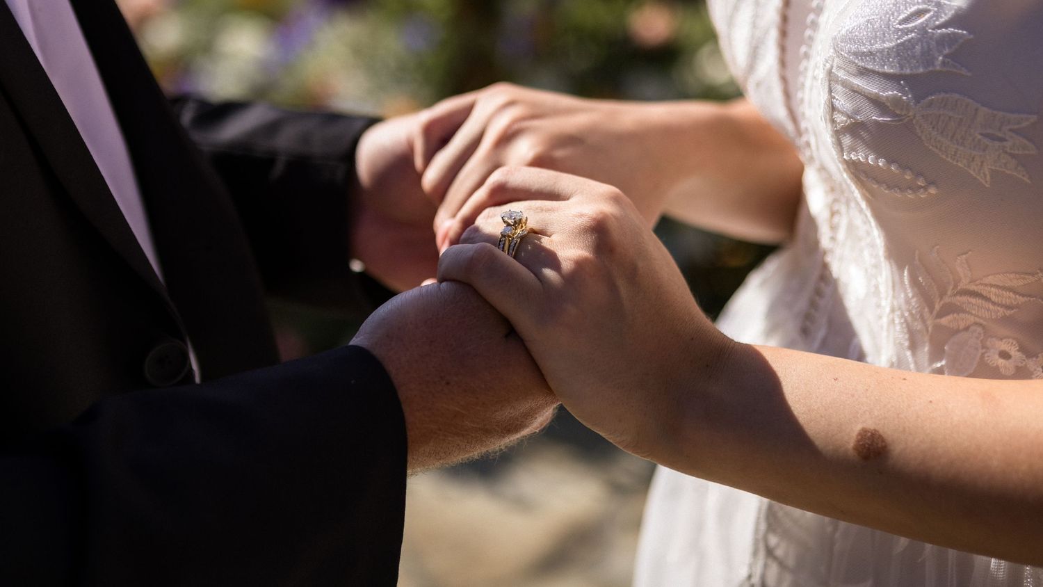 Close-up of bride and groom exchanging rings during wedding ceremony, showcasing diamond engagement ring.