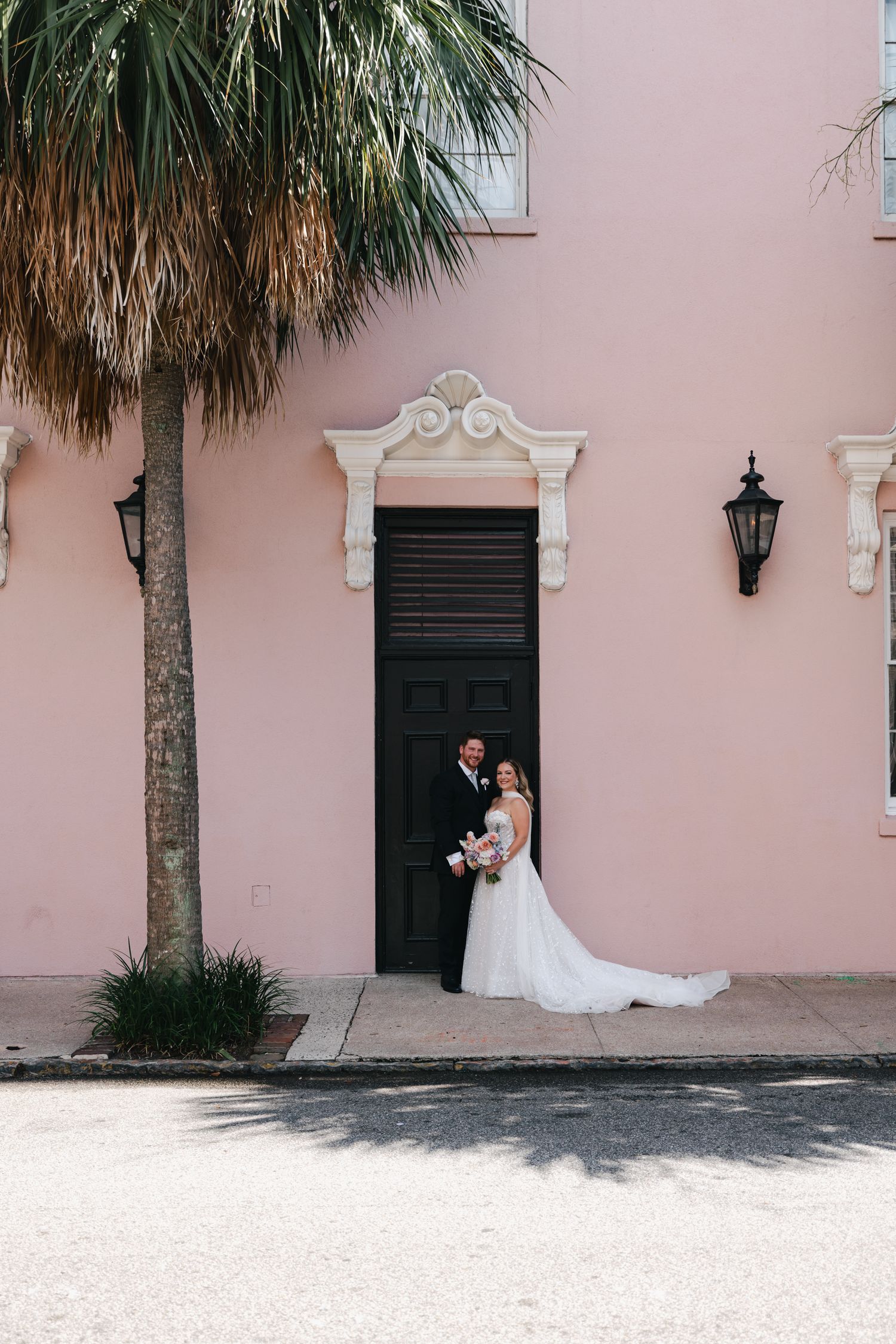 Bride and groom posing in front of a pink building with a black door in Charleston, SC.