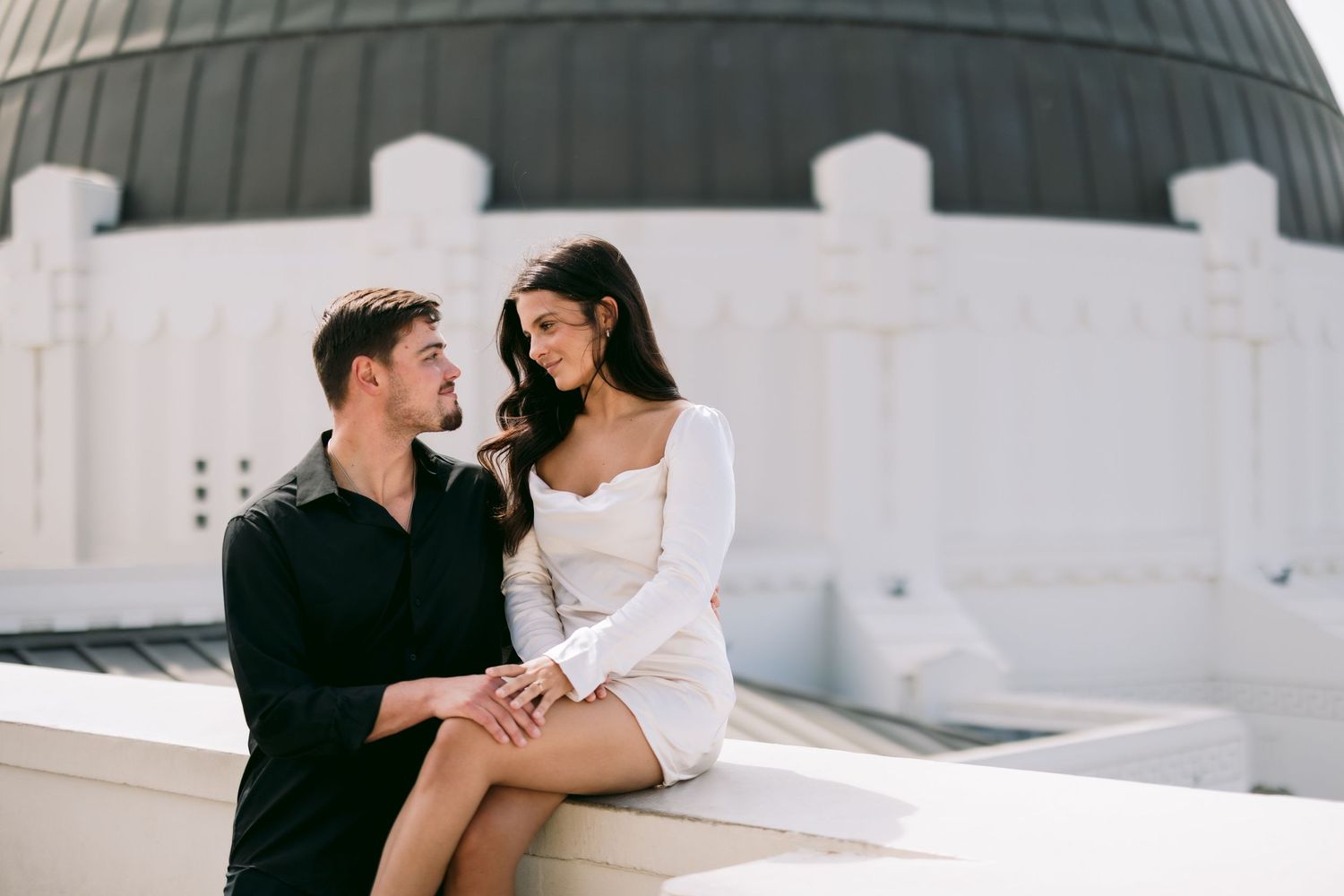 Couple sitting close together on white ledge at Griffith Observatory in Los Angeles.
