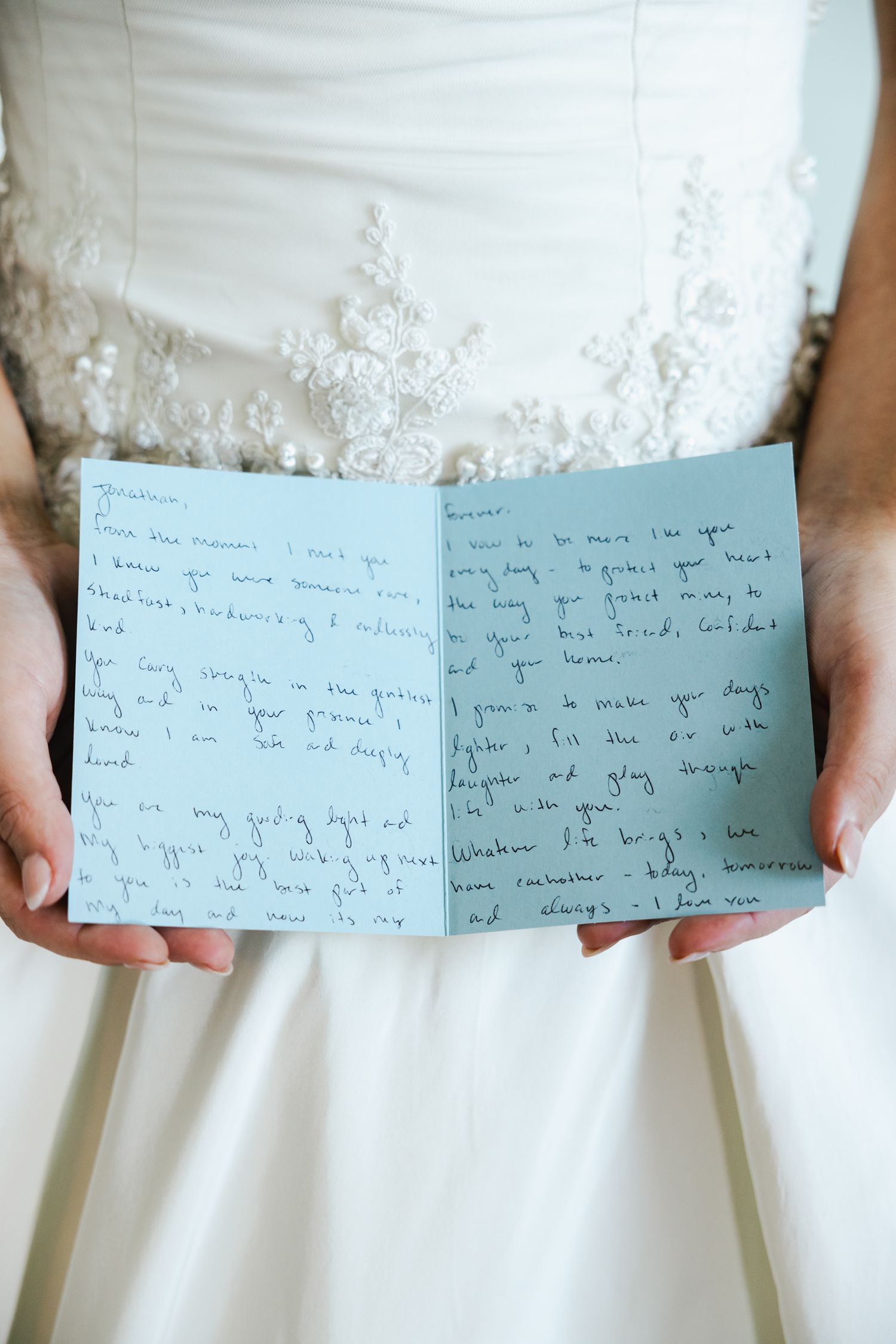Bride in lace wedding gown holds handwritten love letter on blue paper during wedding day preparations.