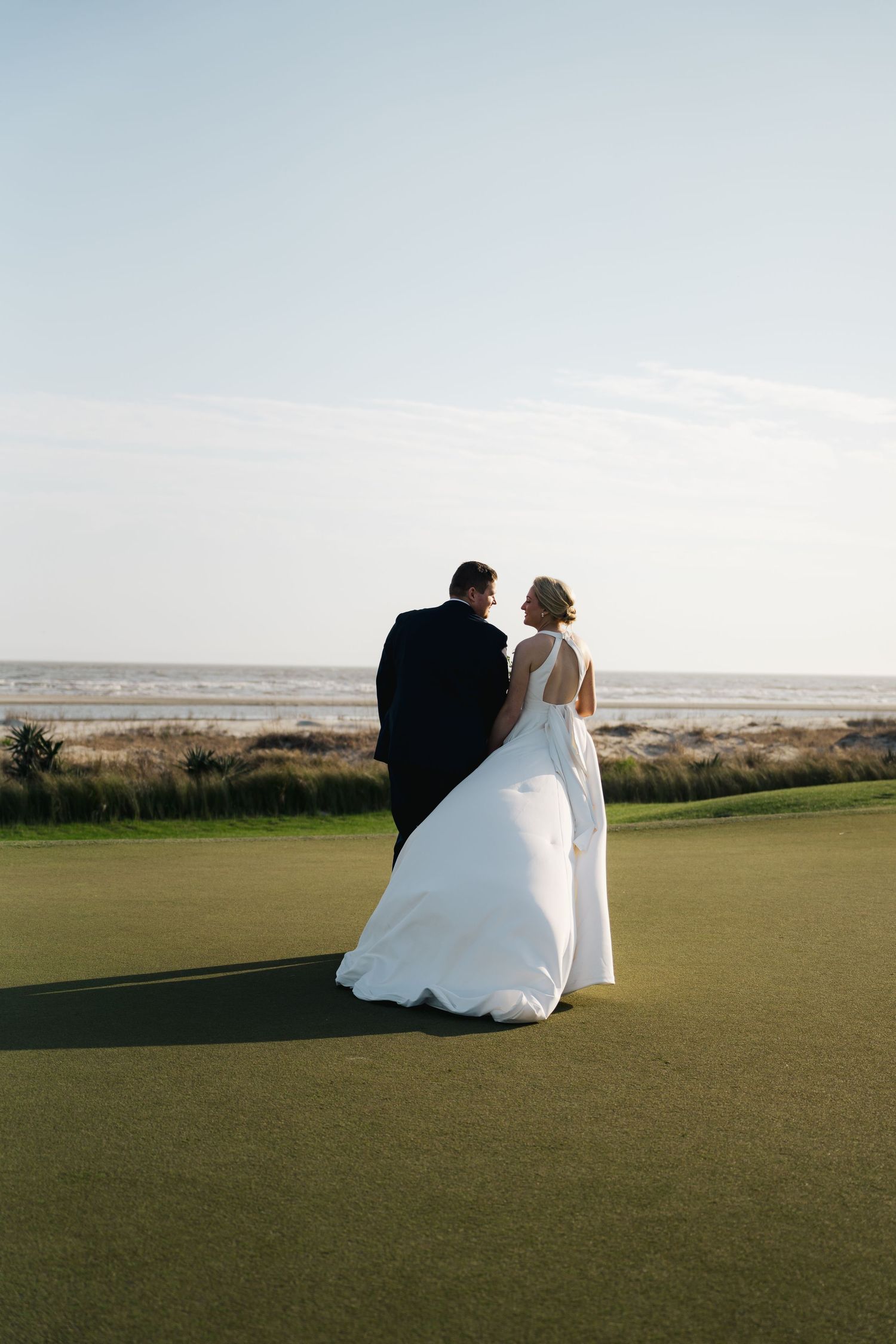Bride and groom stand together on a lush golf course overlooking the ocean on their wedding day.