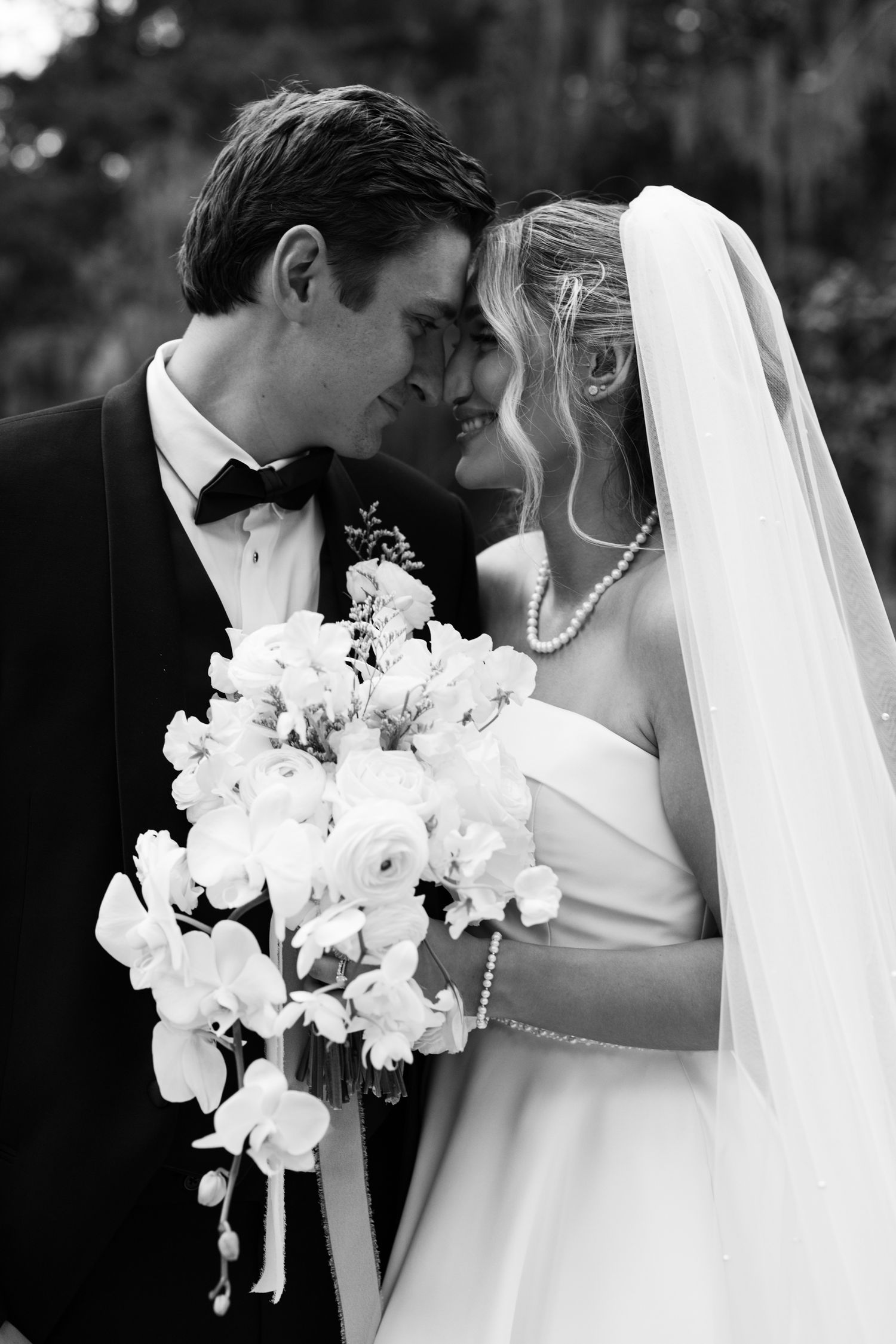 Black and white portrait of a bride and groom sharing an intimate moment, bride holding a white floral bouquet.