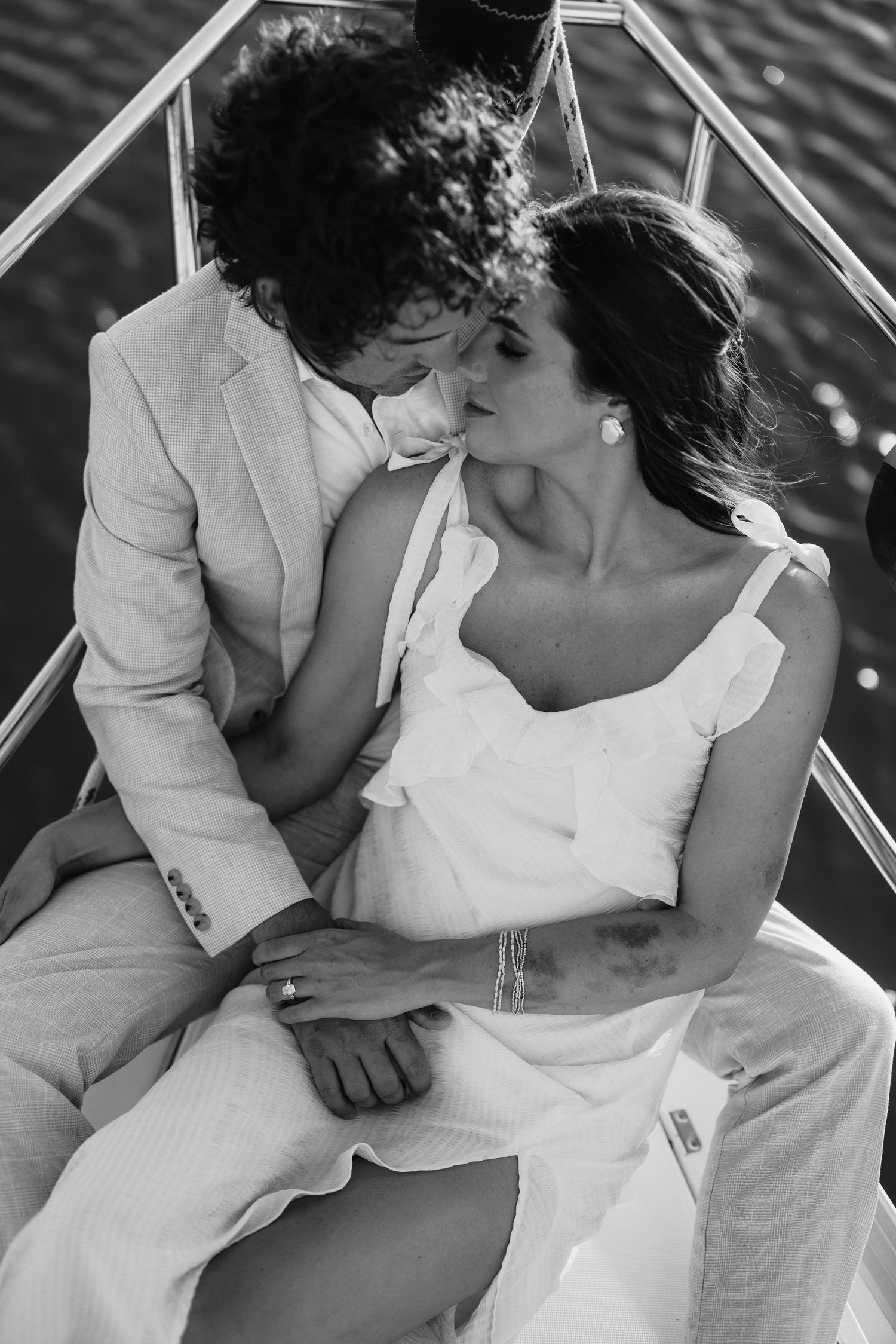 Black and white photo of a couple in wedding attire sharing a romantic moment on a boat.