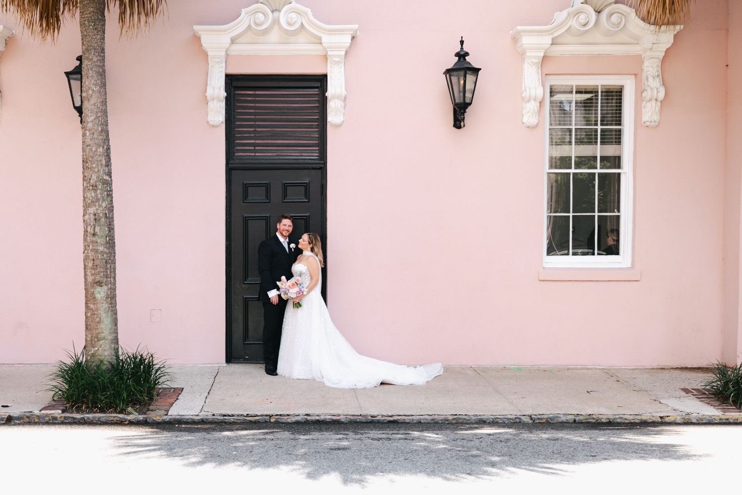 Bride and groom pose in front of a charming pink building with black door in Charleston, SC wedding portrait.