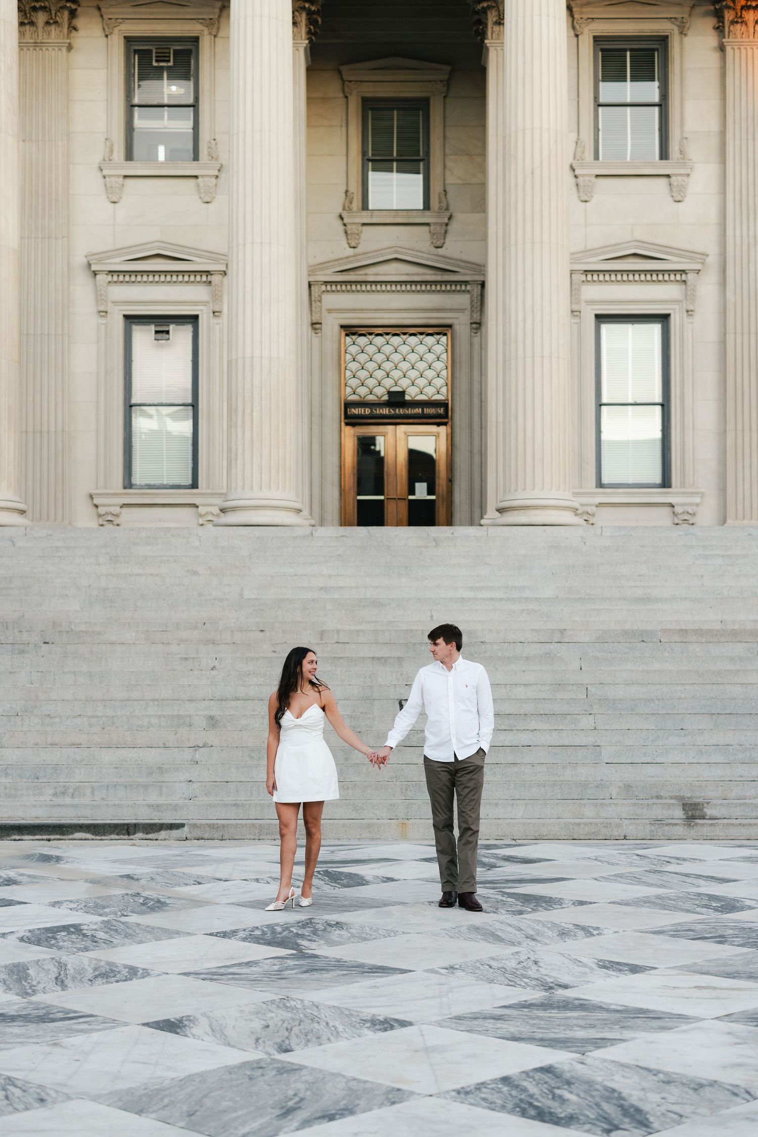 Couple holding hands on the marble steps of a grand neoclassical building with tall columns.
