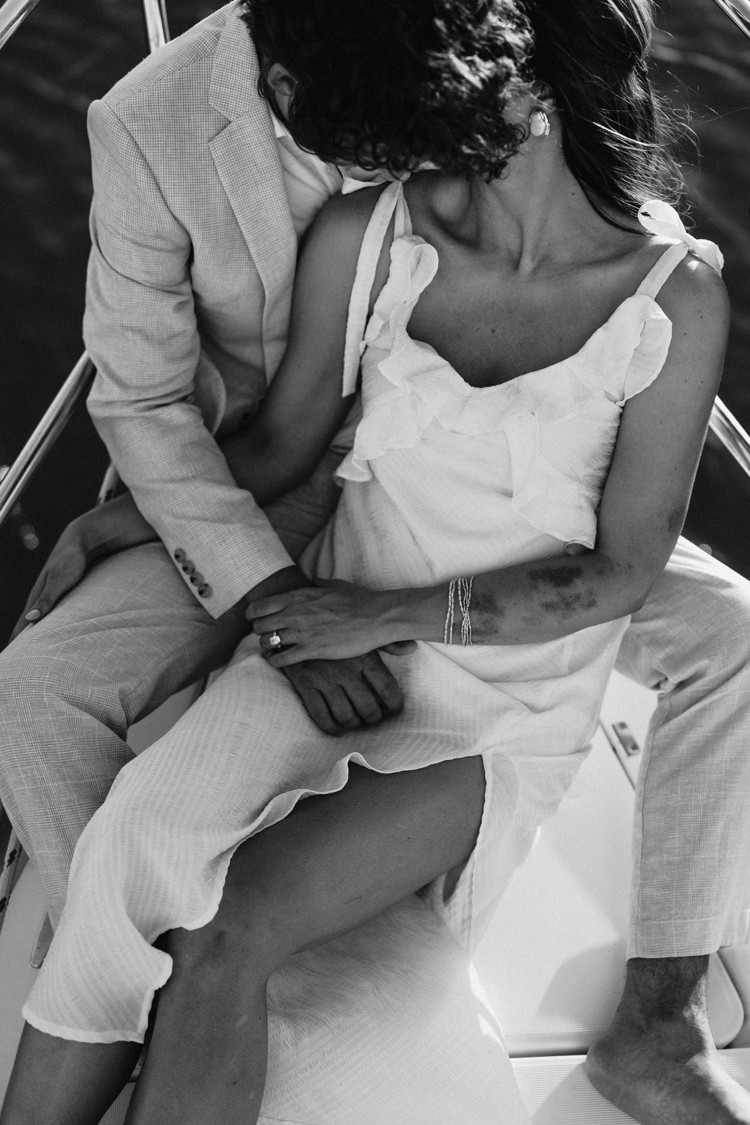 Black and white close-up of a couple sitting intimately together on a sailboat deck holding hands.