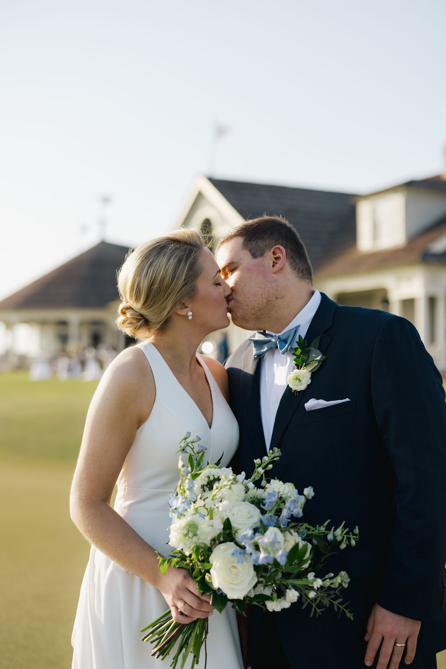 Bride and groom sharing a kiss outdoors, bride holding white and blue floral bouquet on wedding day.
