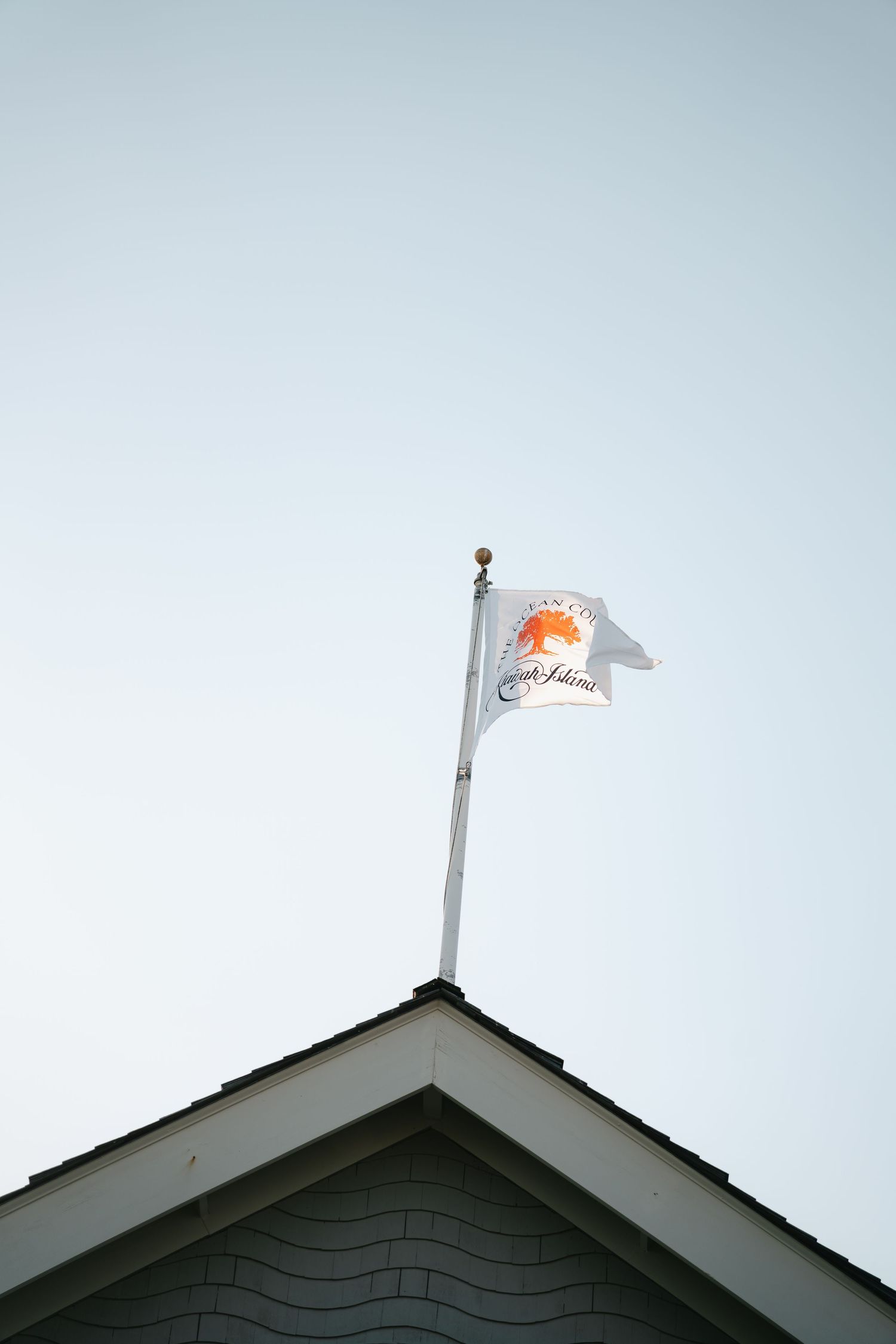 A white flag with an orange logo flies atop a building's peaked roof against a clear sky.