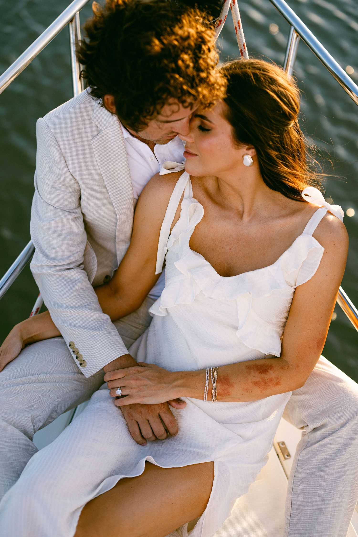 Romantic couple in elegant white attire sharing an intimate moment on the bow of a sailboat.