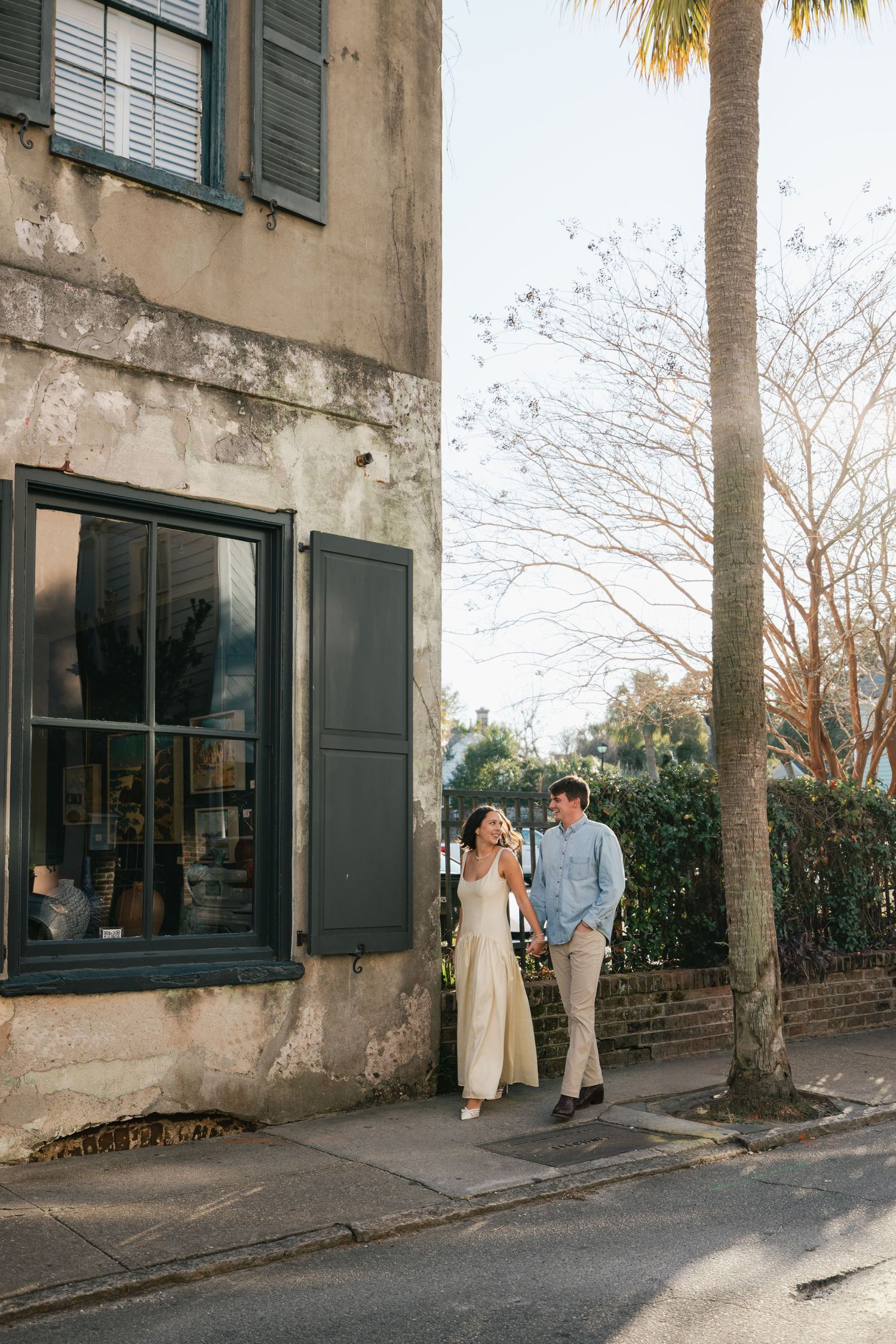 Couple walking and laughing together on a charming historic street with aged building and palm tree.
