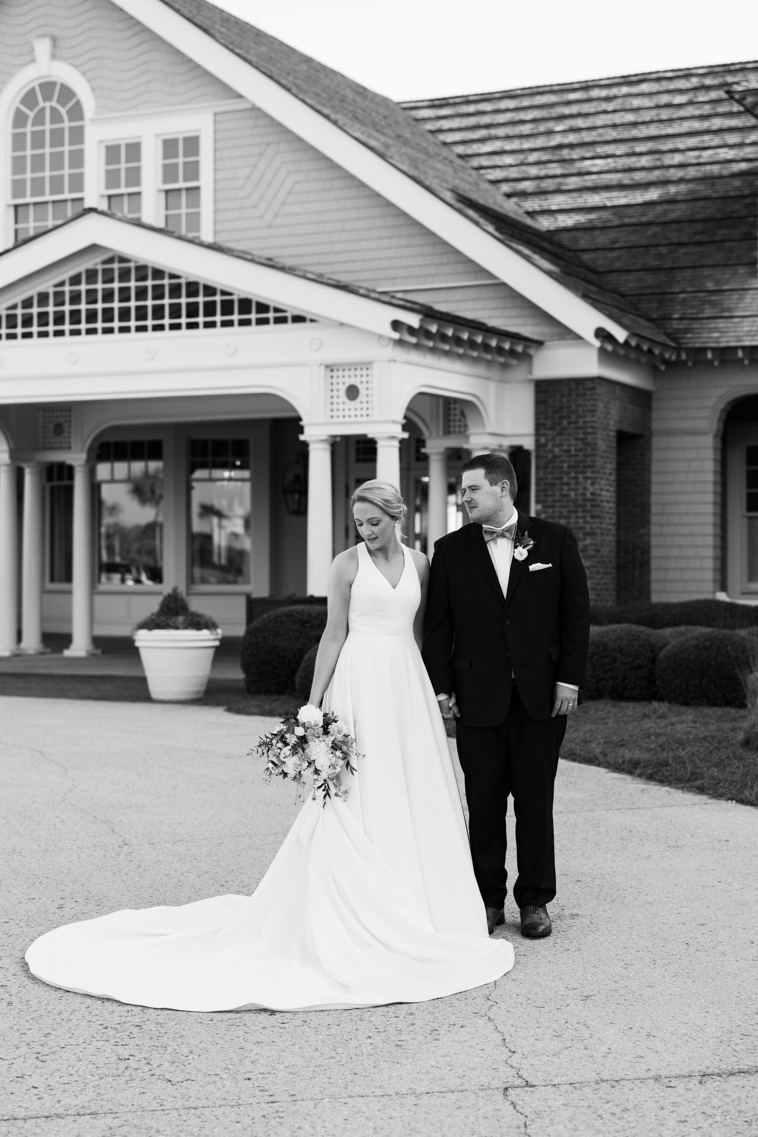 Bride and groom walking in black and white photo outside wedding venue building.