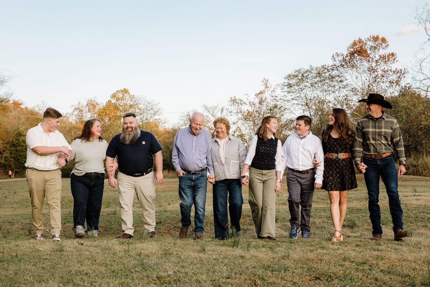 Large family group walking together outdoors in a field during golden hour, smiling and holding hands.