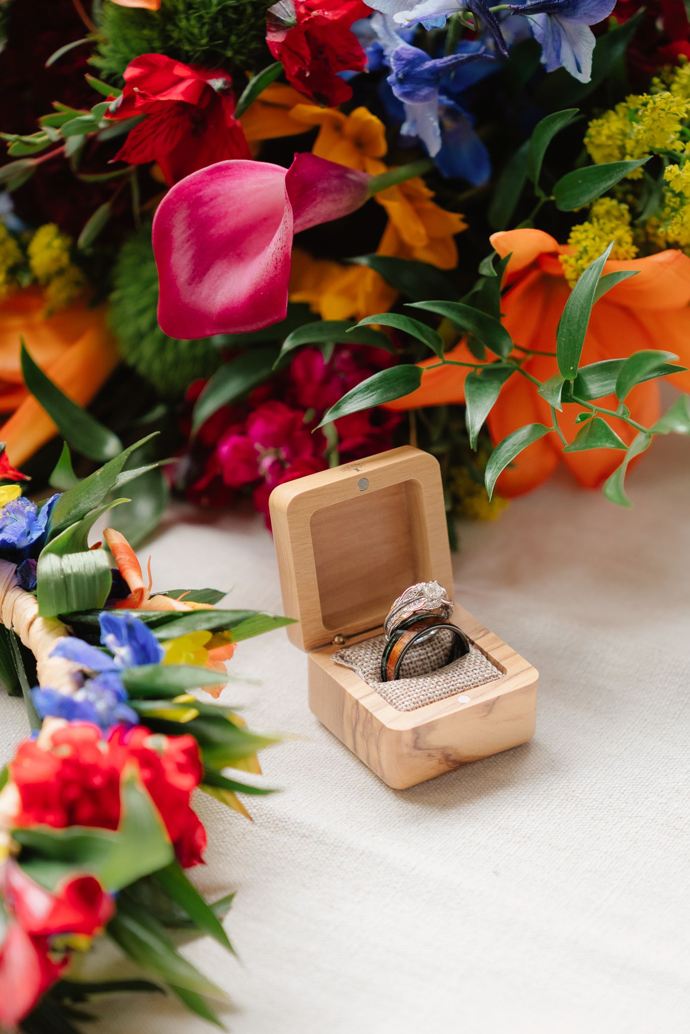 Diamond engagement ring in wooden box surrounded by vibrant colorful wedding bouquets with pink, orange, and blue flowers.