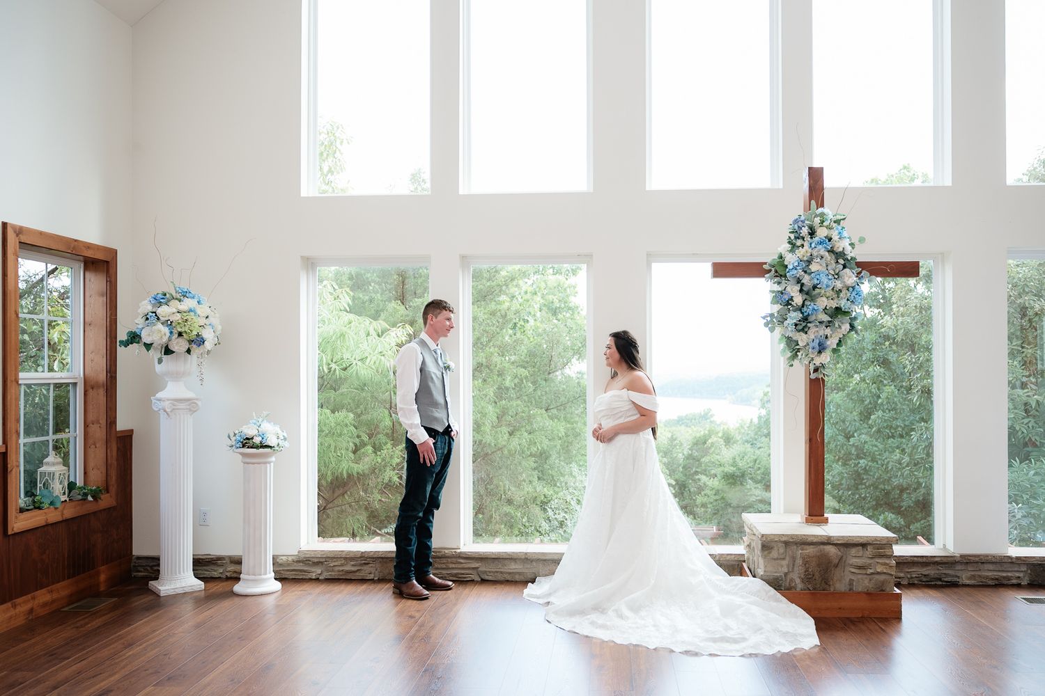 Bride and groom share a first look moment in an elegant chapel with large windows and blue floral arrangements.