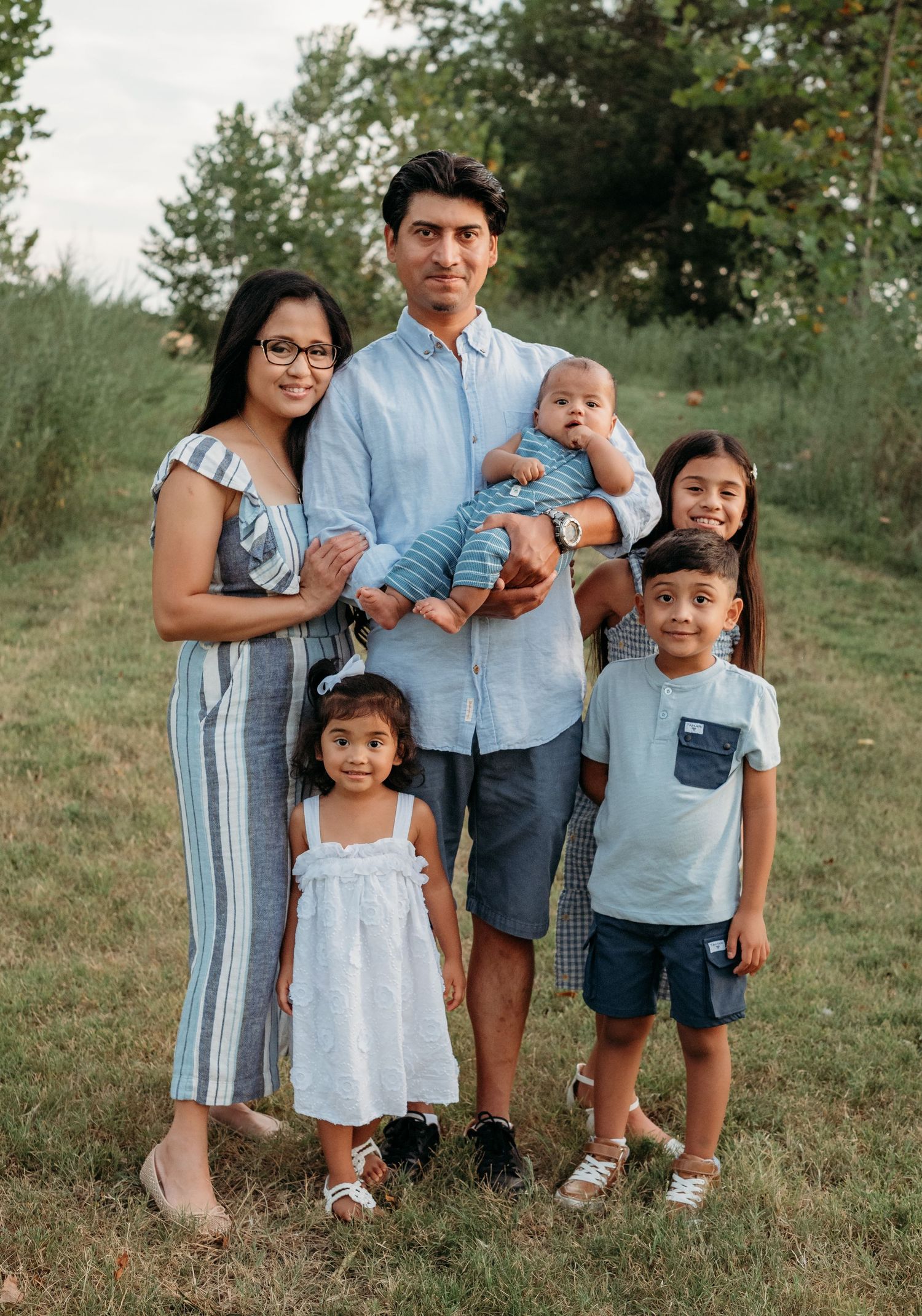 Happy family of six posing outdoors in a green field during a warm summer evening.