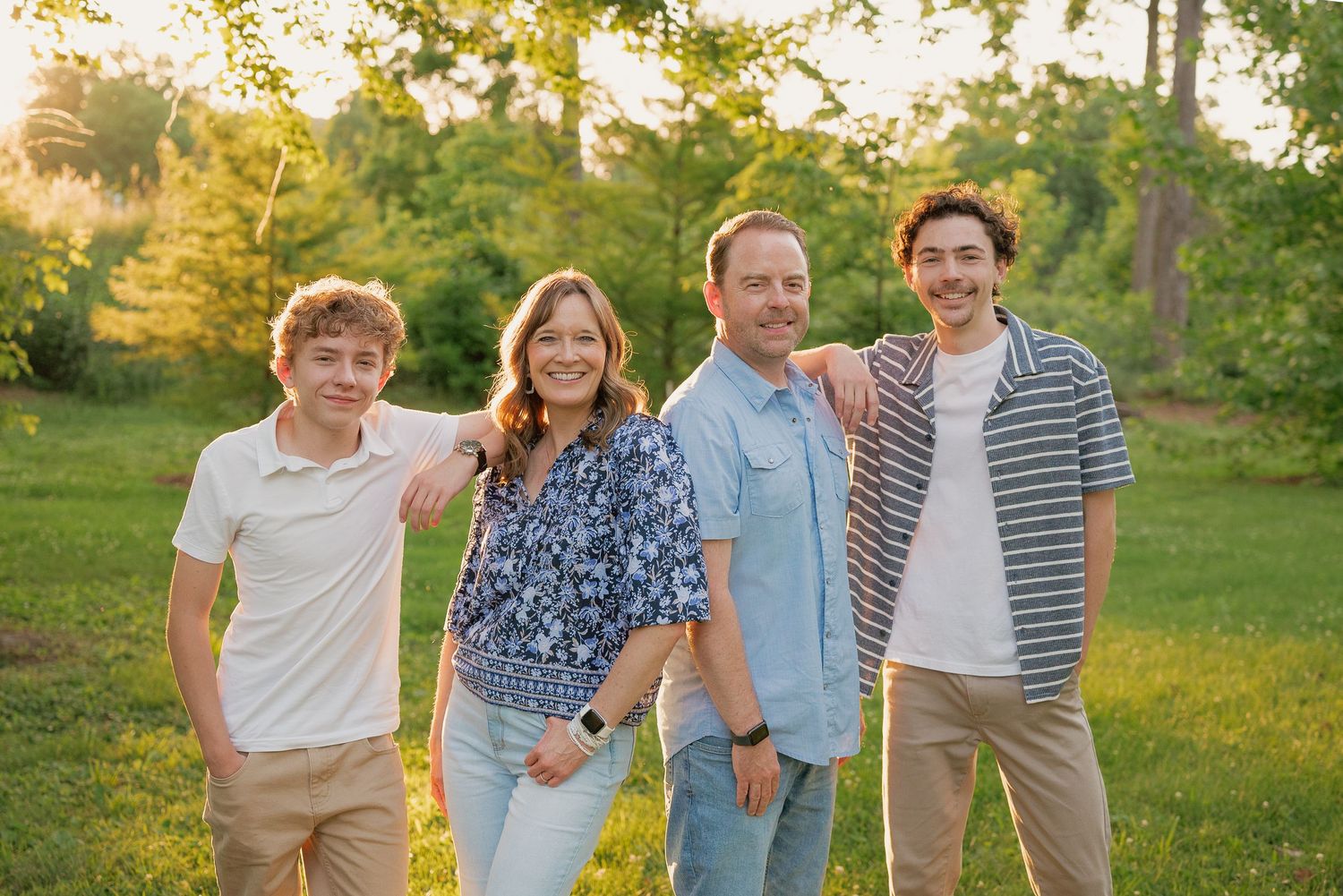 Happy family of four posing together on a lush green lawn at golden hour.