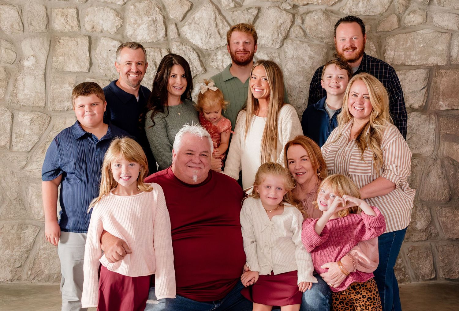 Large multigenerational family portrait smiling together in front of a stone wall backdrop.