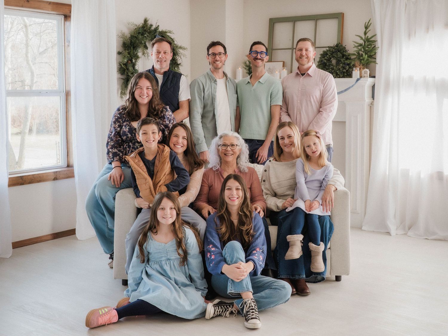 Large family group portrait smiling together in a bright, decorated living room with holiday greenery.