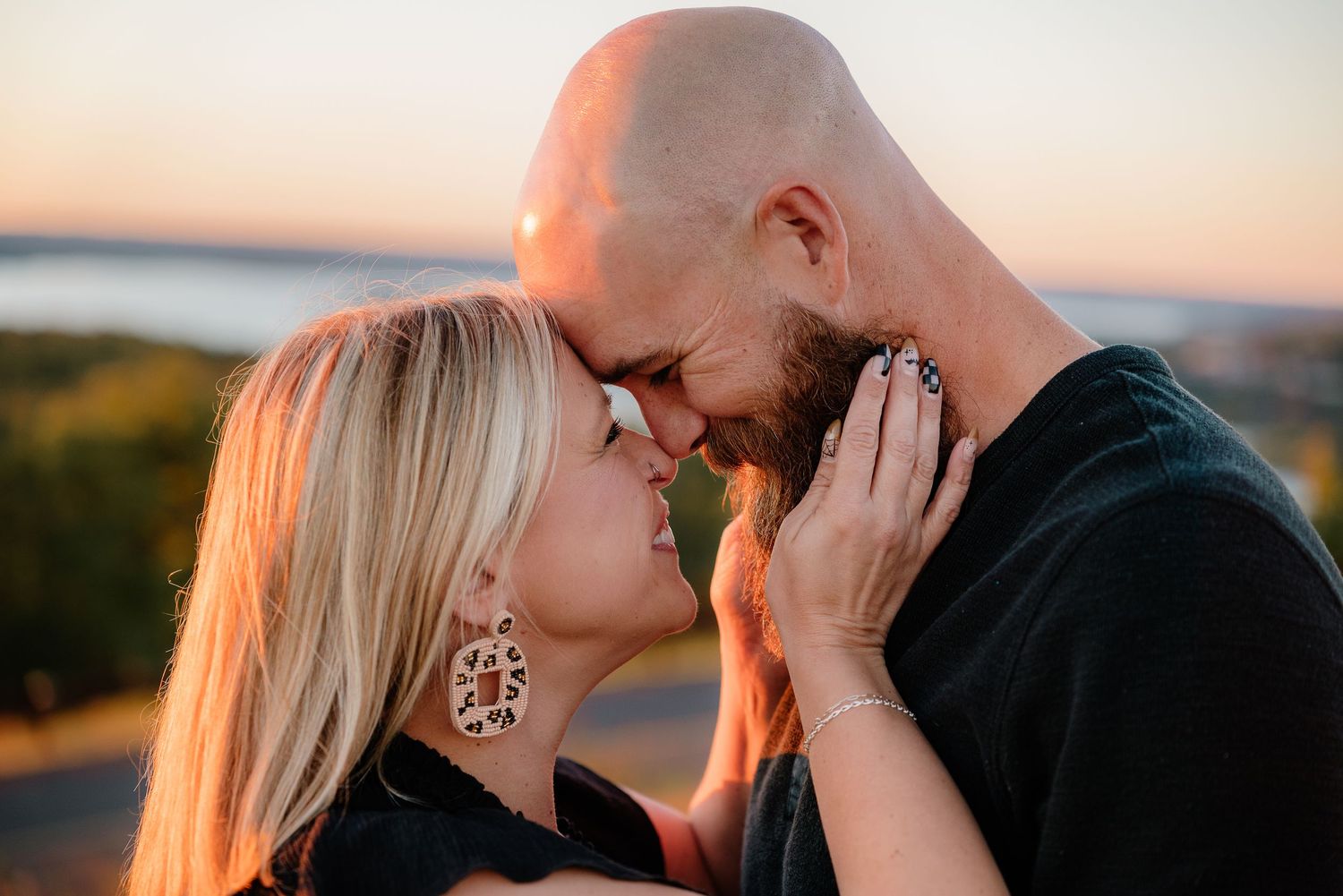 Romantic couple sharing an intimate moment at sunset, touching foreheads, woman wearing decorative earrings outdoors.
