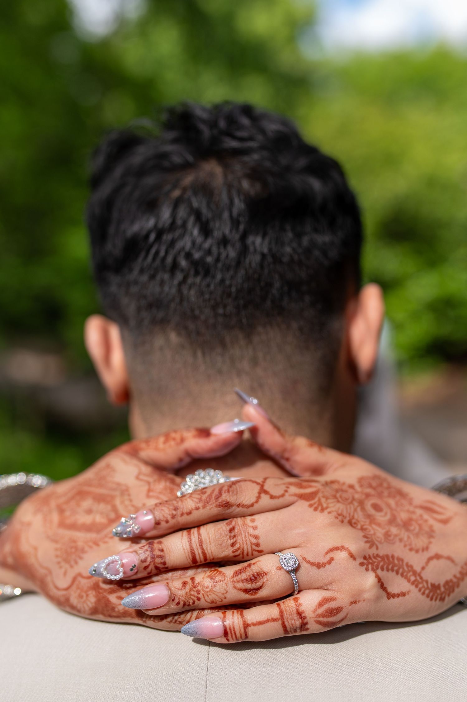 Close-up of bride's henna-decorated hands resting on groom's neck at outdoor wedding in london.