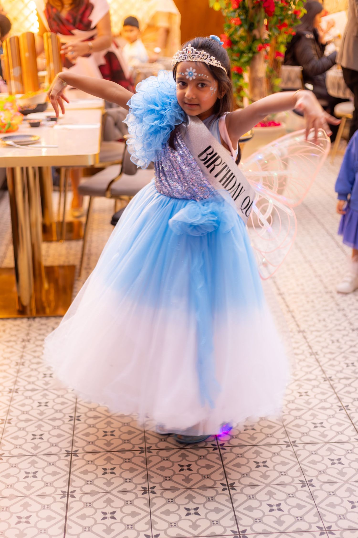 Young girl in blue princess gown with birthday sash and tiara dancing at a birthday party celebration in London