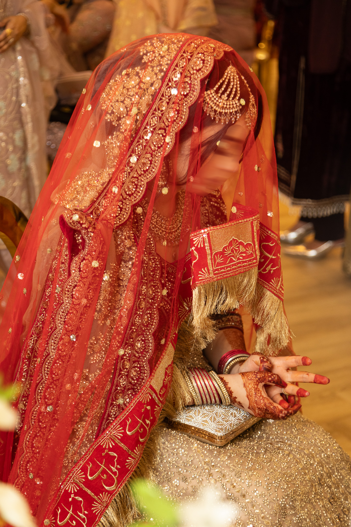 Muslim bride in red embroidered dupatta bowing over Quran receitation during traditional Nikah ceremony in London.
