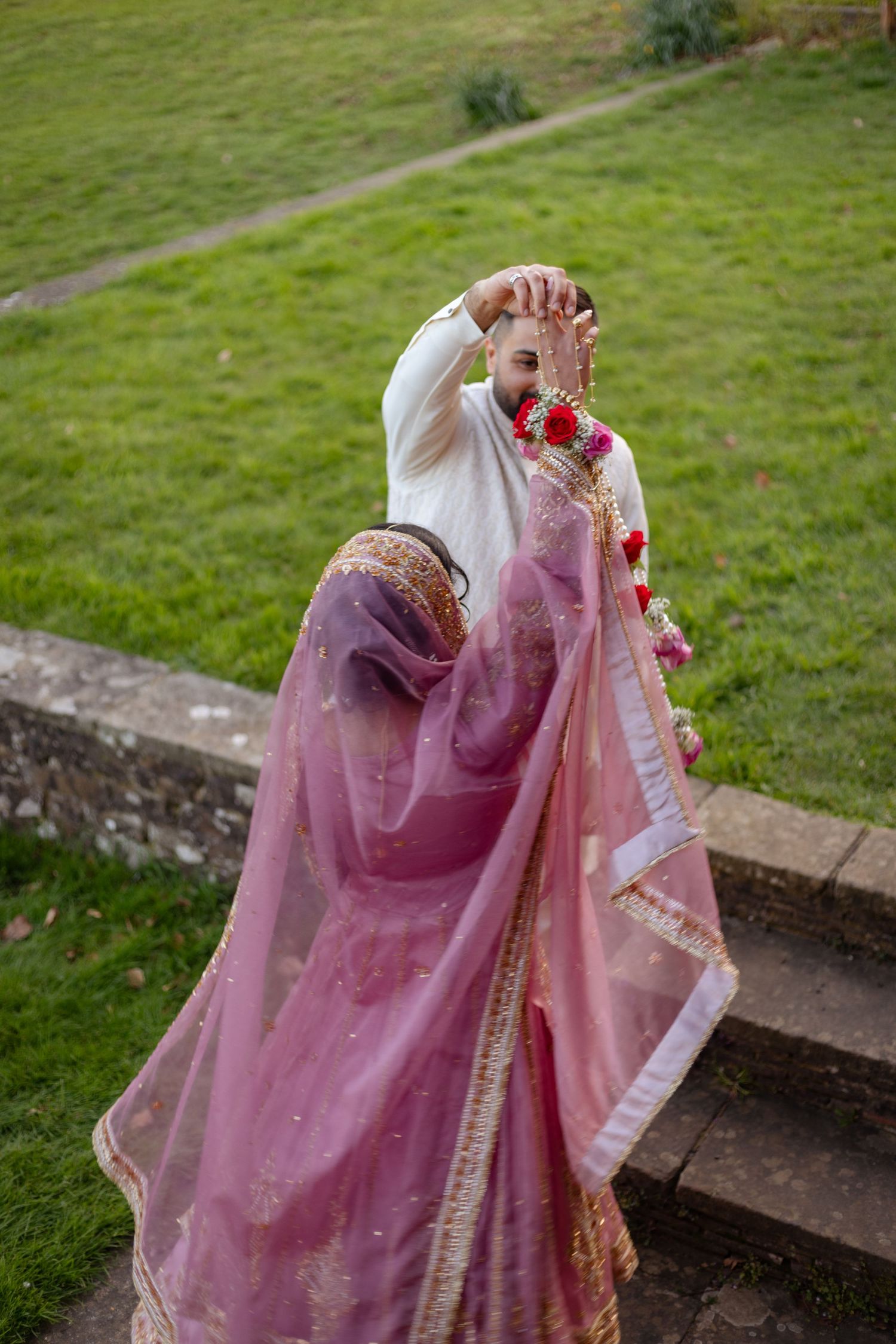 Pakistani bride in pink lehenga twirling on outdoor steps with green lawn background in london.