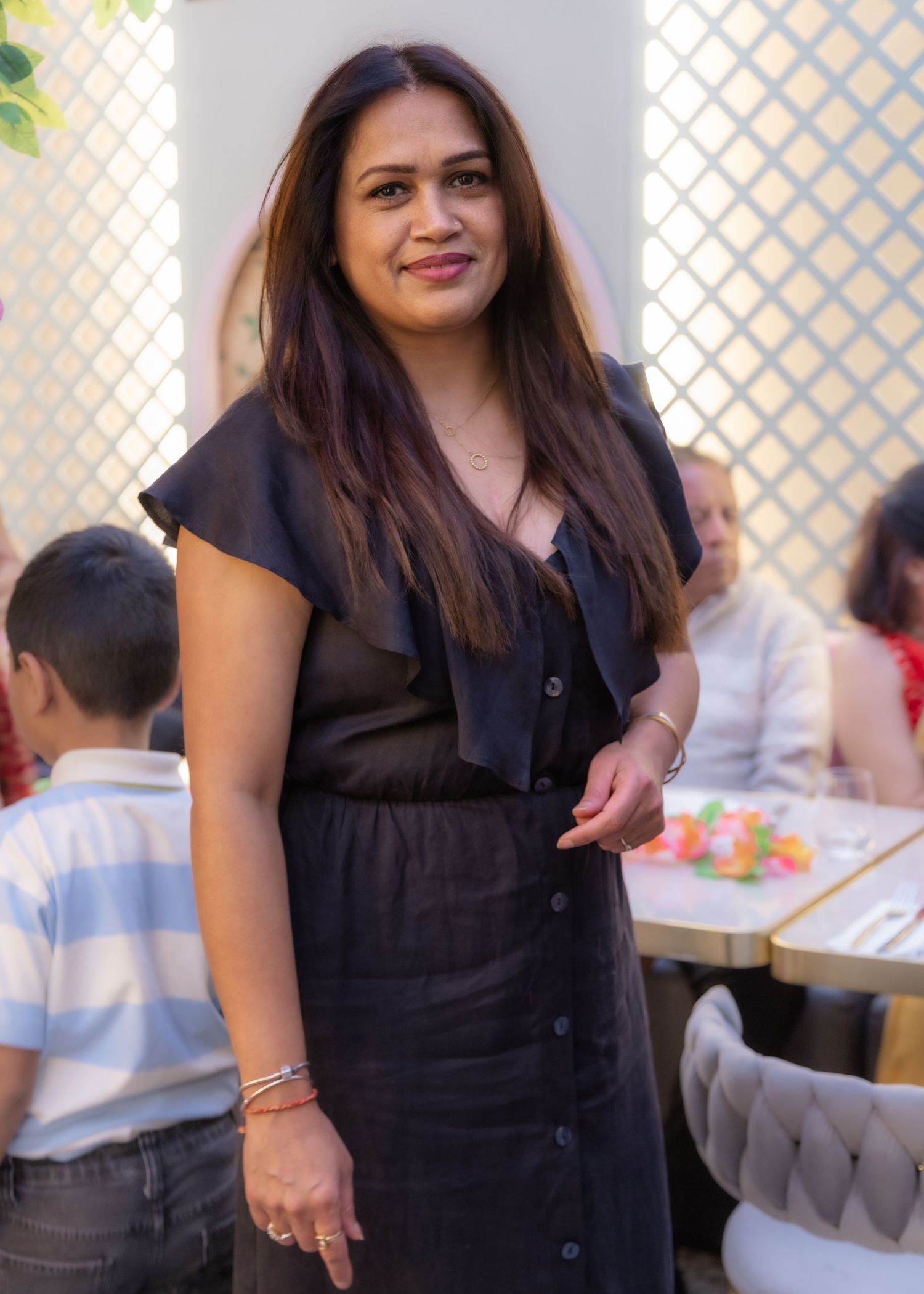 A woman in a dark dress smiles while standing in a bright restaurant setting at a birthday event in Hounslow.