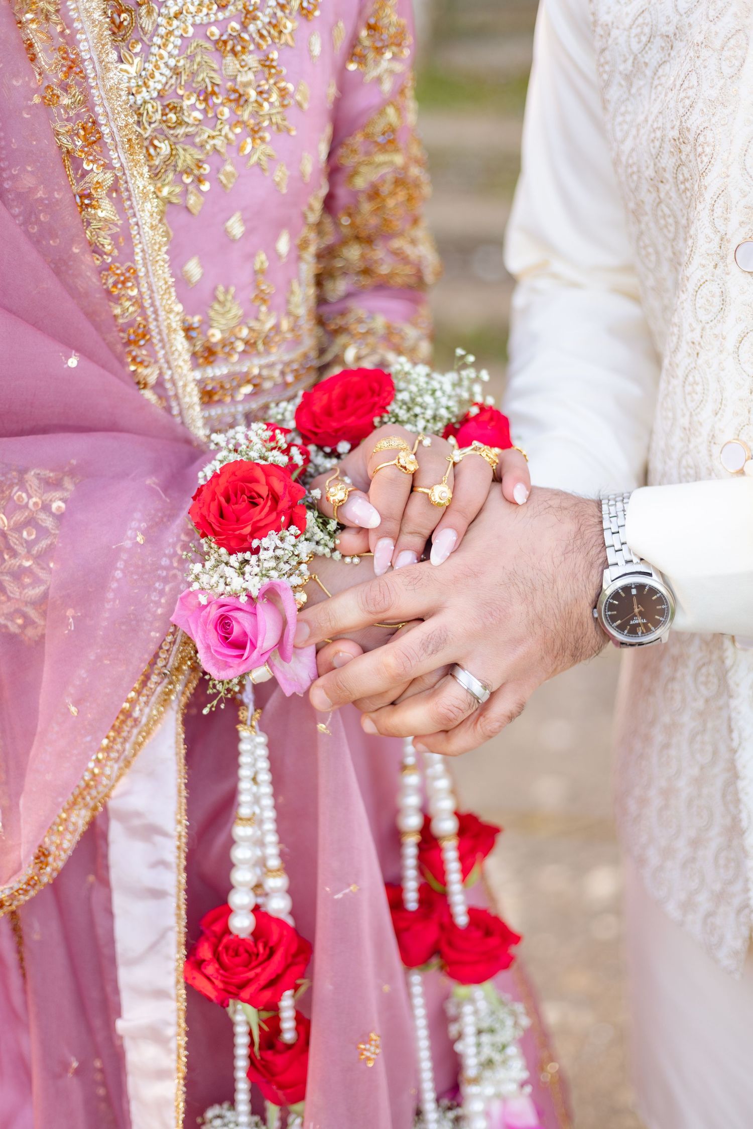 South Asian couple hold hands adorned with roses and pearl garland during wedding ceremony in london.