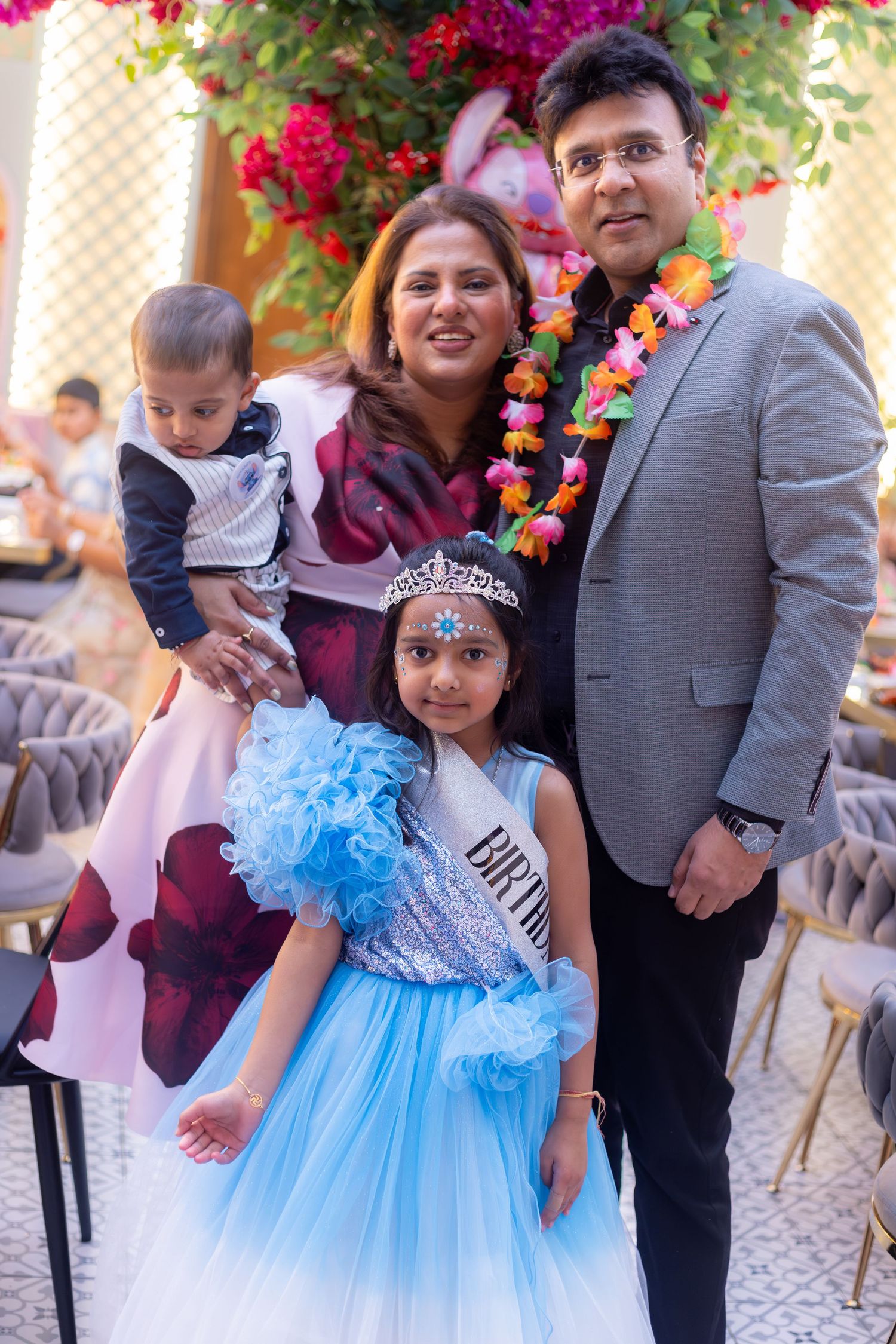 Family celebrating a birthday party, girl in blue tutu dress with tiara, parents and baby posing outdoors in London