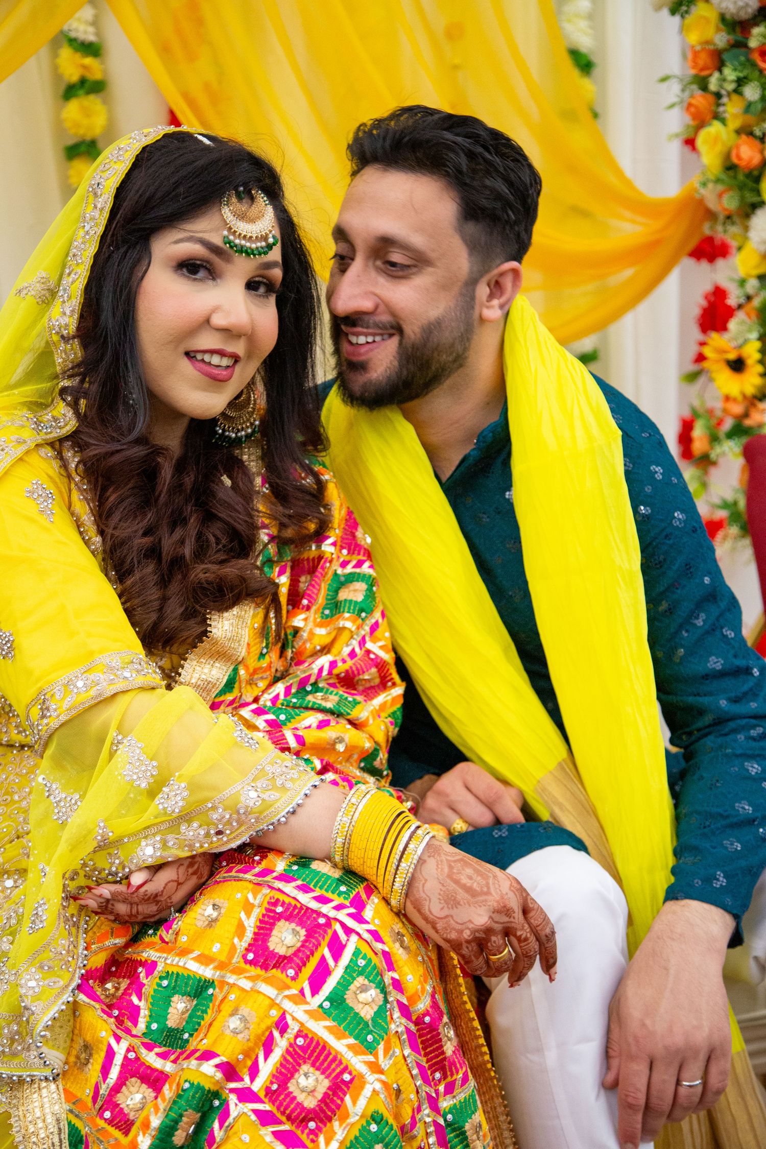 South Asian couple in vibrant yellow and multicolor traditional wedding attire smiling together in London.