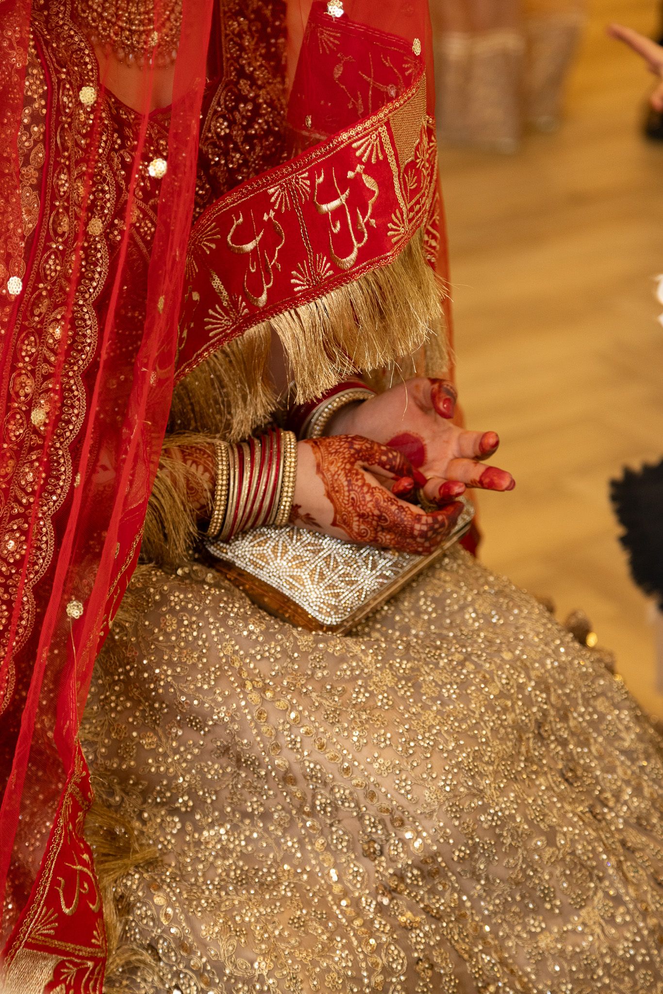 Close-up of Muslim bride in red lehenga with henna-adorned hands and bangles in London.
