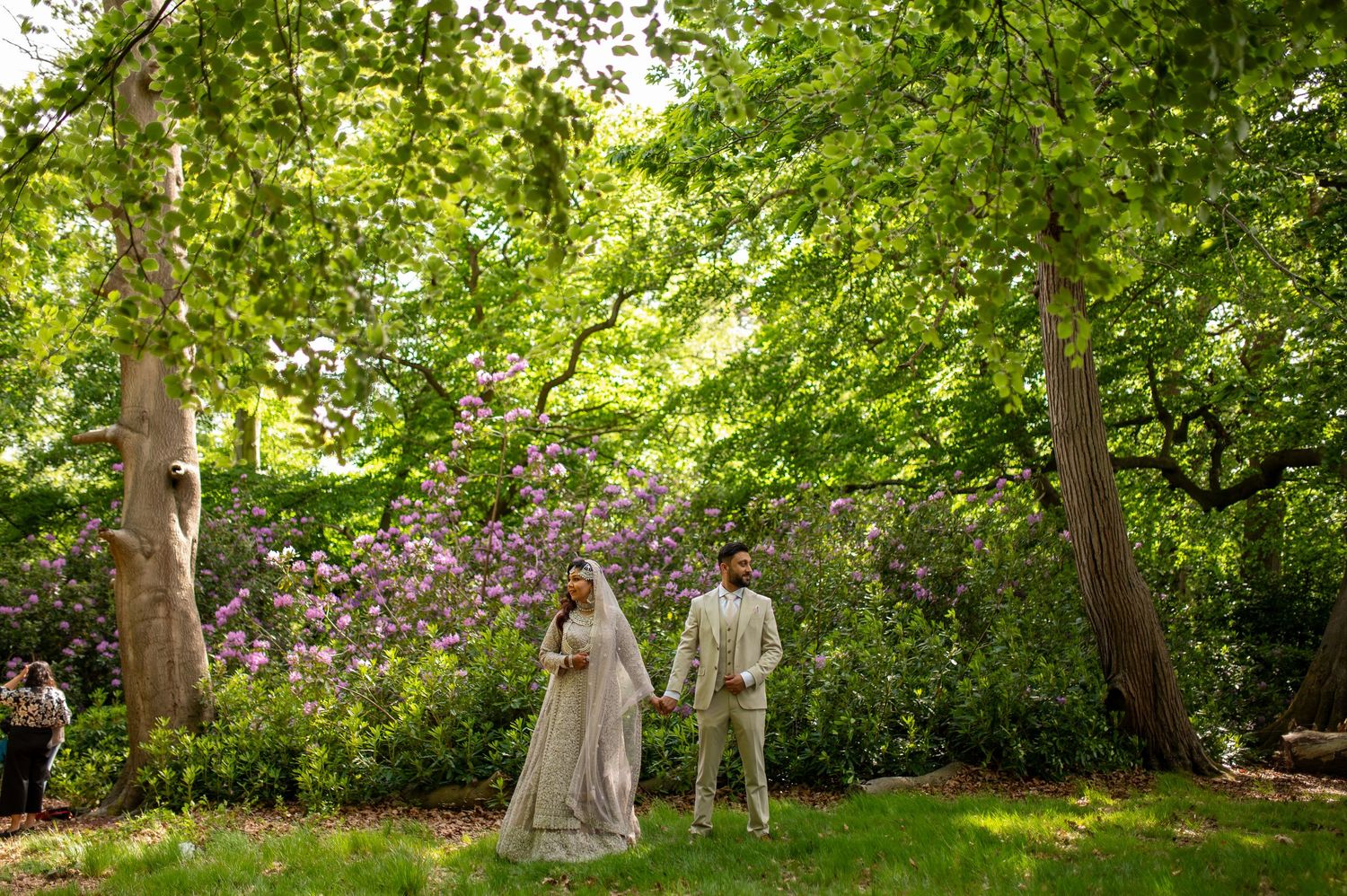 Bride and groom standing in a lush green garden with blooming purple flowers during an outdoor wedding ceremony in london.