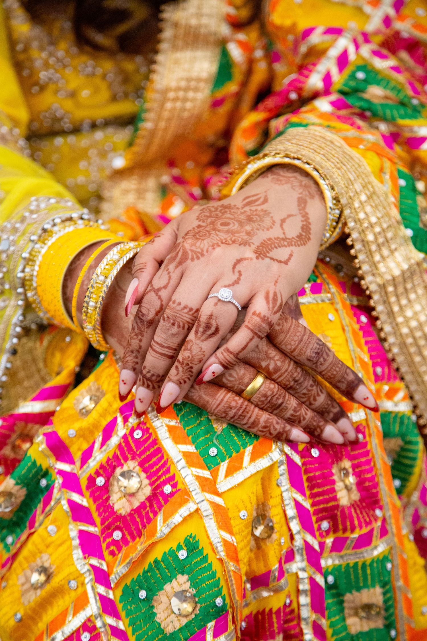 Pakistani Bride's hands with intricate henna mehndi design and diamond ring on colorful embroidered fabric in London